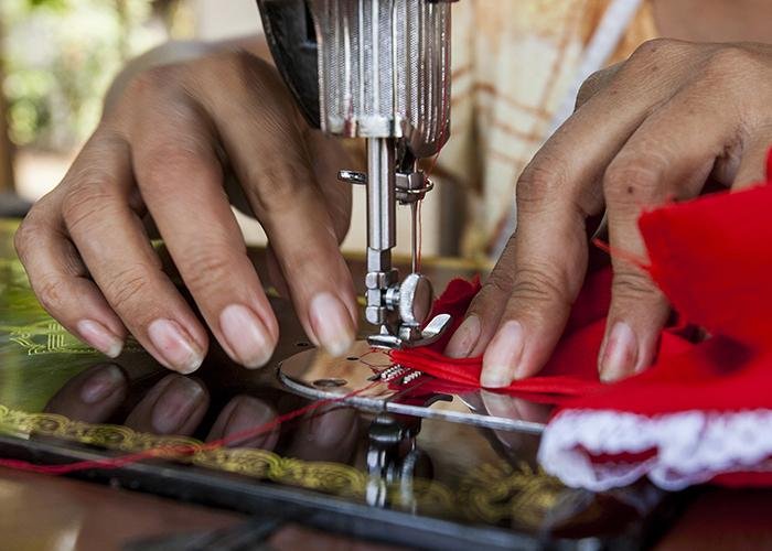Close-up of person's hands guiding red fabric through a sewing machine.