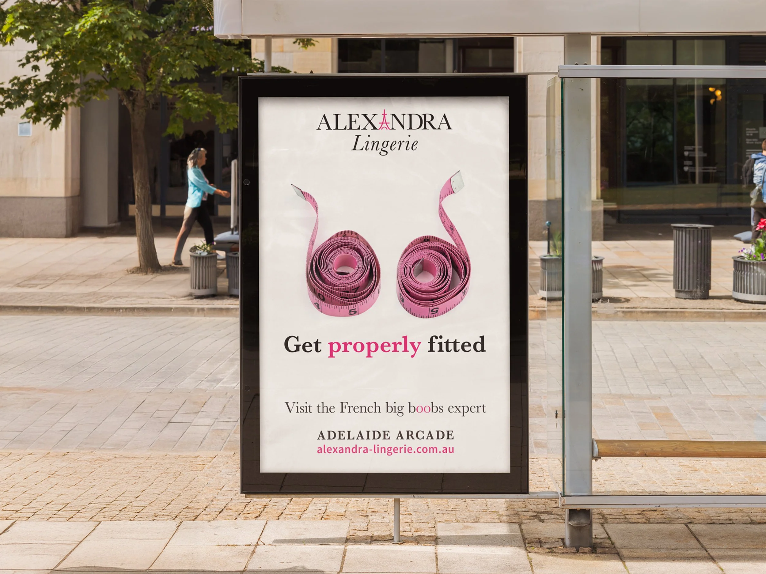 Advertisement poster for Alexandra Lingerie featuring two pink measuring tapes shaped like swans, with text promoting proper fitting and mentioning an expert at Adelaide Arcade.