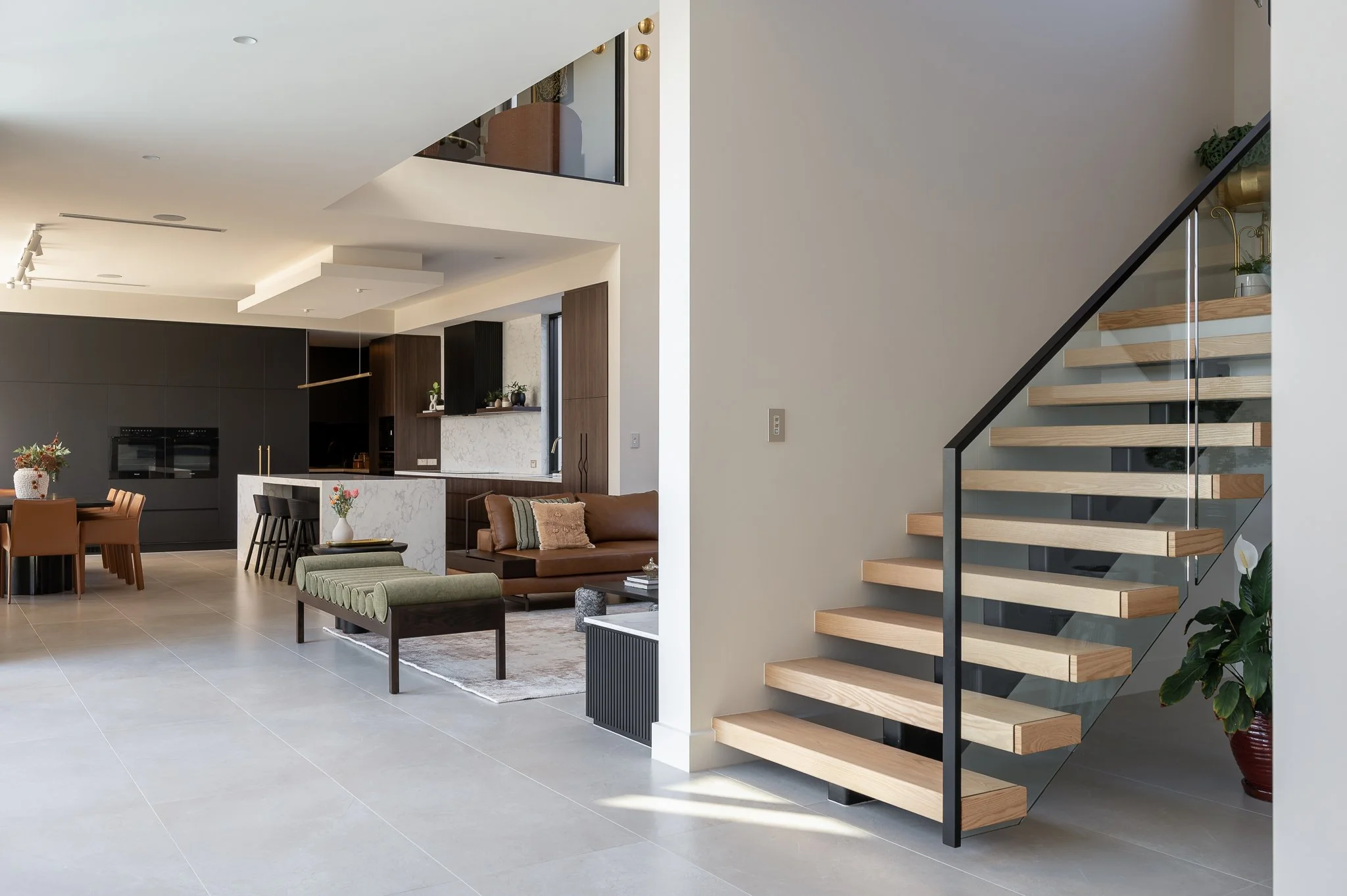 Modern open plan area, with a staircase to the right and lounge / kitchen visible in the background.