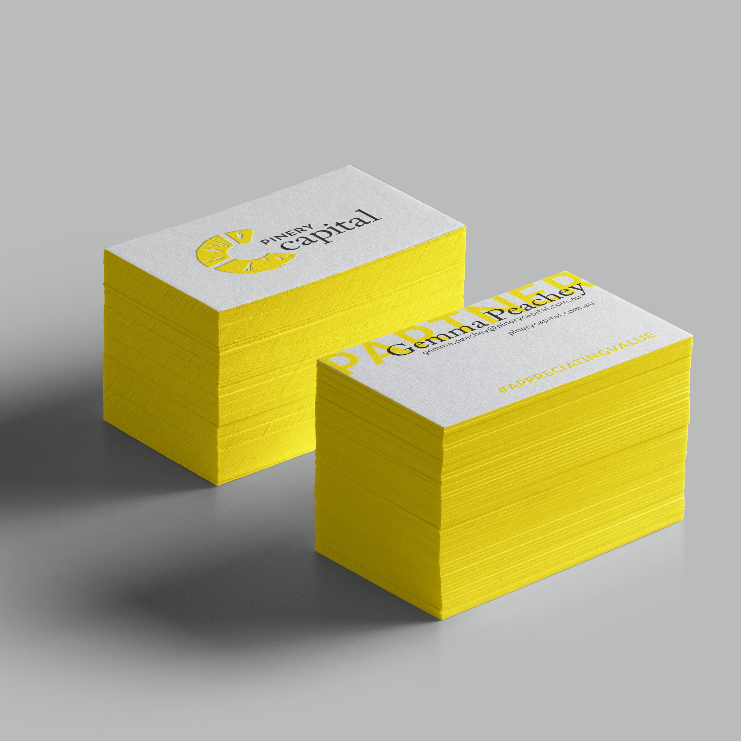 Stacks of yellow business cards with white tops featuring black and yellow text and logos, placed on a gray surface.