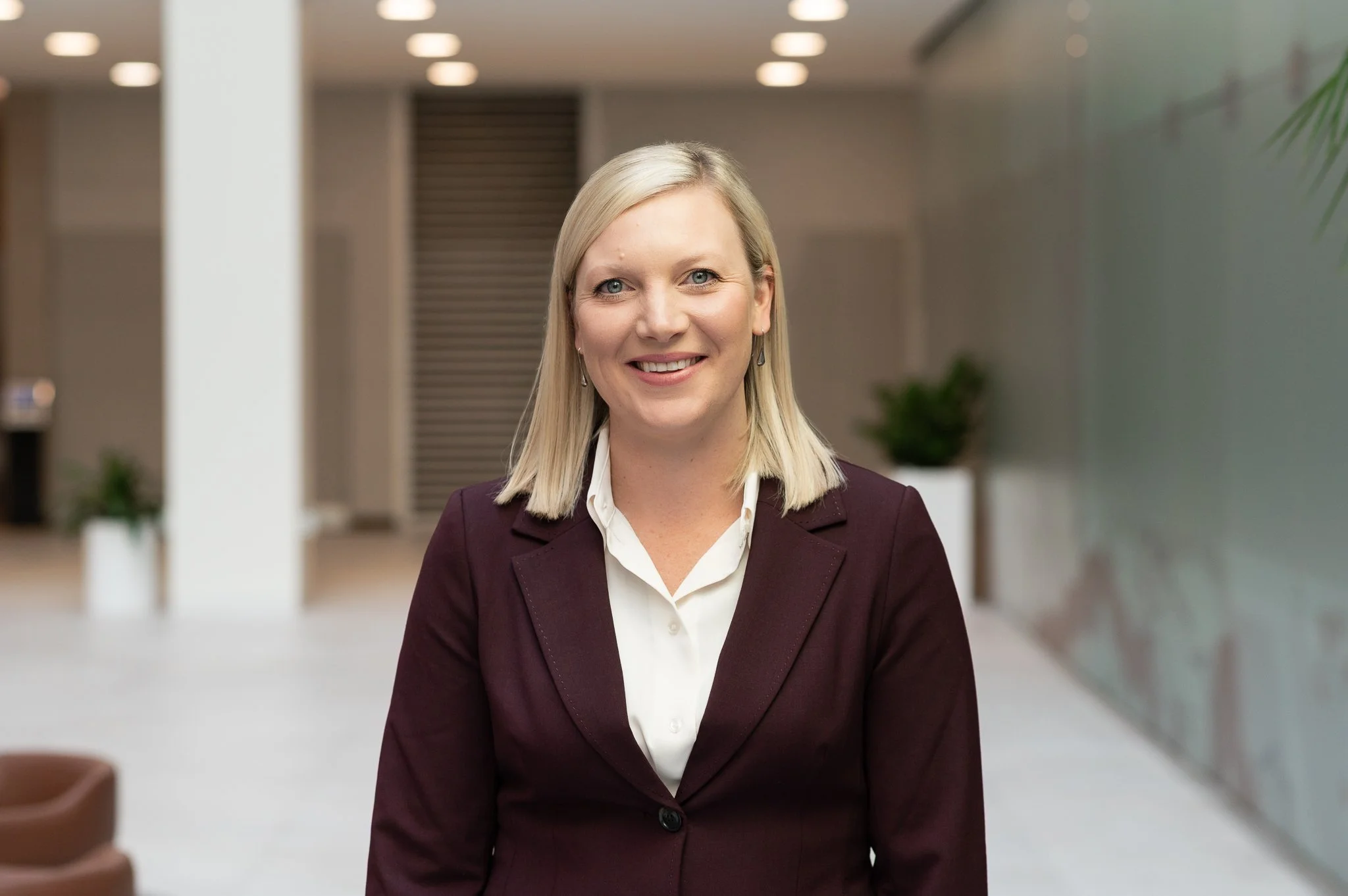 A professional woman with blonde hair smiling in an office environment.