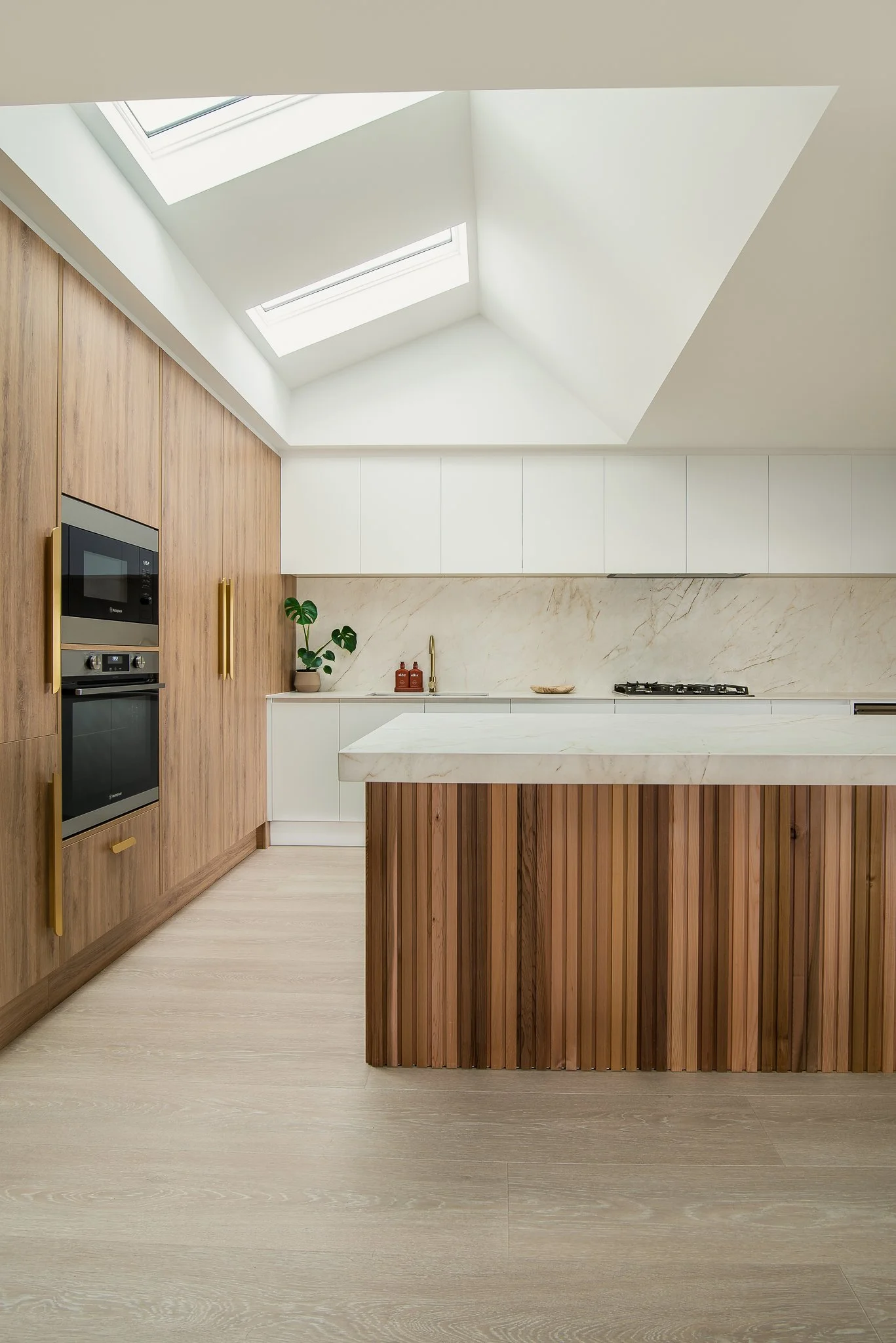 Modern kitchen with wooden and white cabinets, marble countertop and backsplash, built-in oven and microwave, skylight windows.