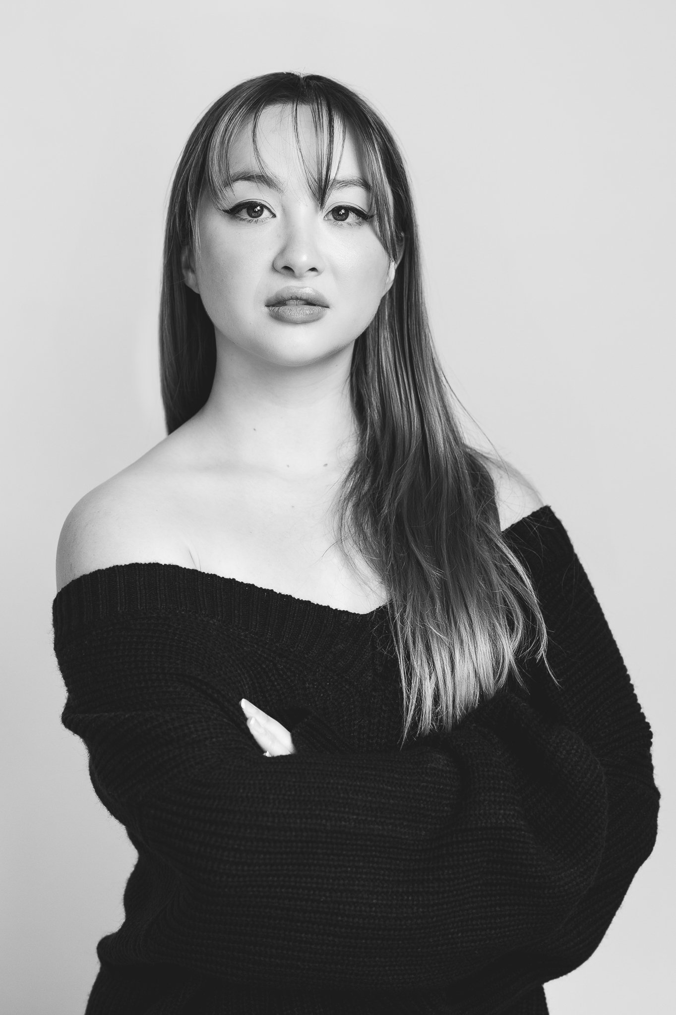 Black and white portrait of a woman with long hair, wearing an off-the-shoulder sweater.