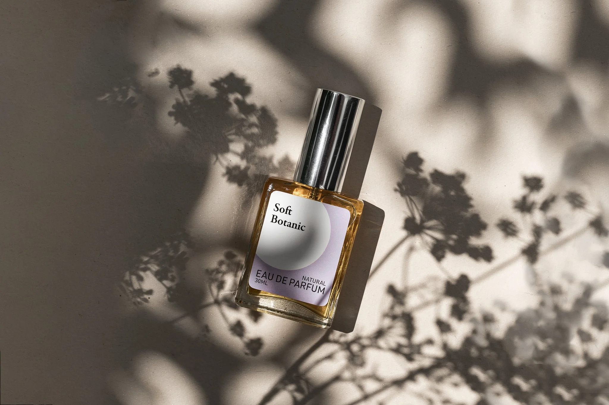 A bottle of Soft Botanic Eau De Parfum on a light surface with shadows of flowers cast around it.
