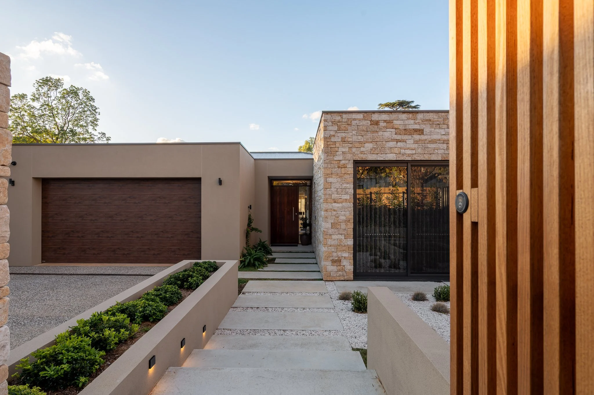 Modern house facade with stone exterior, driveway, and landscaped garden.