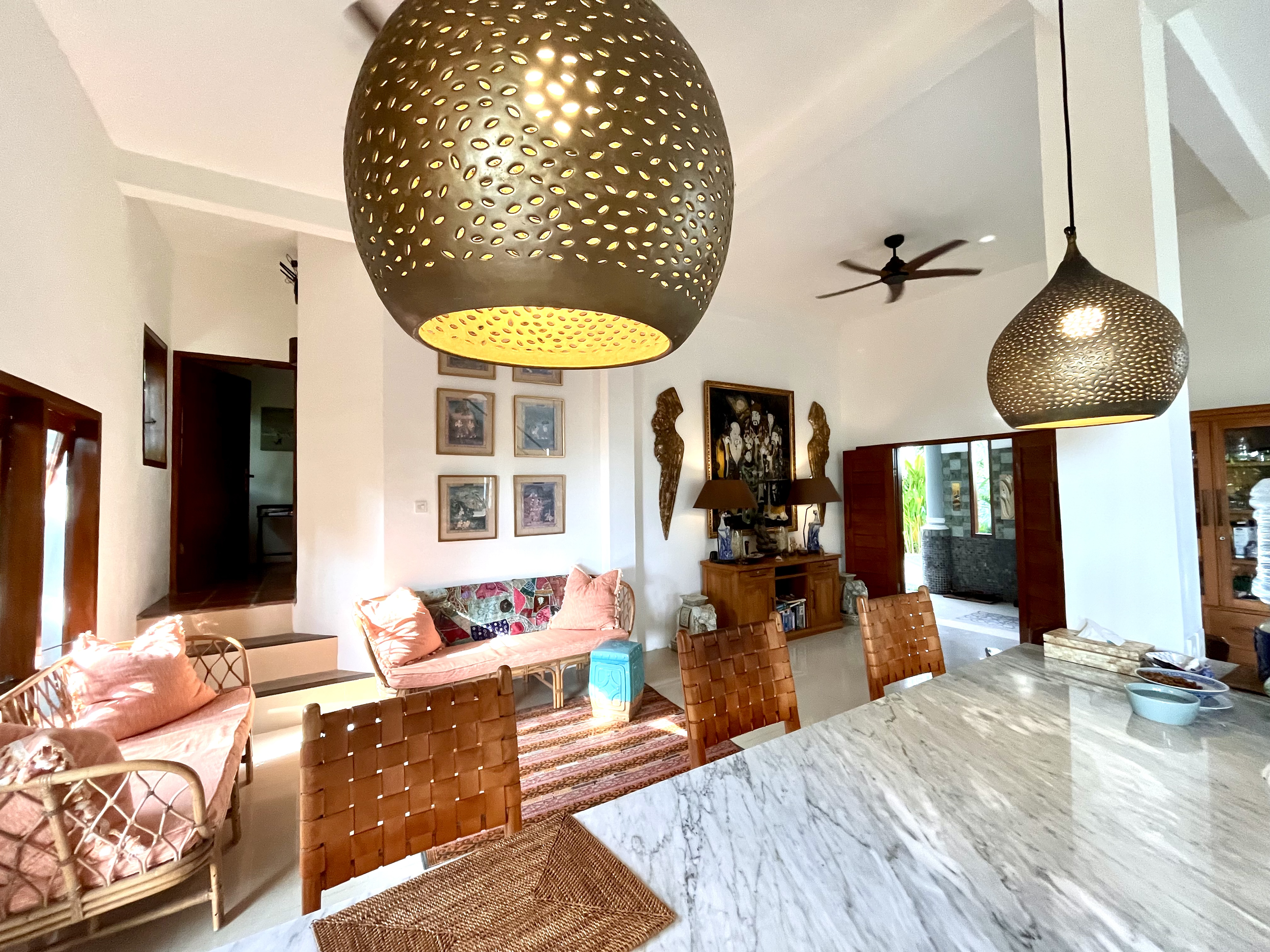 A living room with sweeping 13 foot ceilings and large custom brass pendant lights dappling light over the expansive marble kitchen highlighting the open floor plan living space.