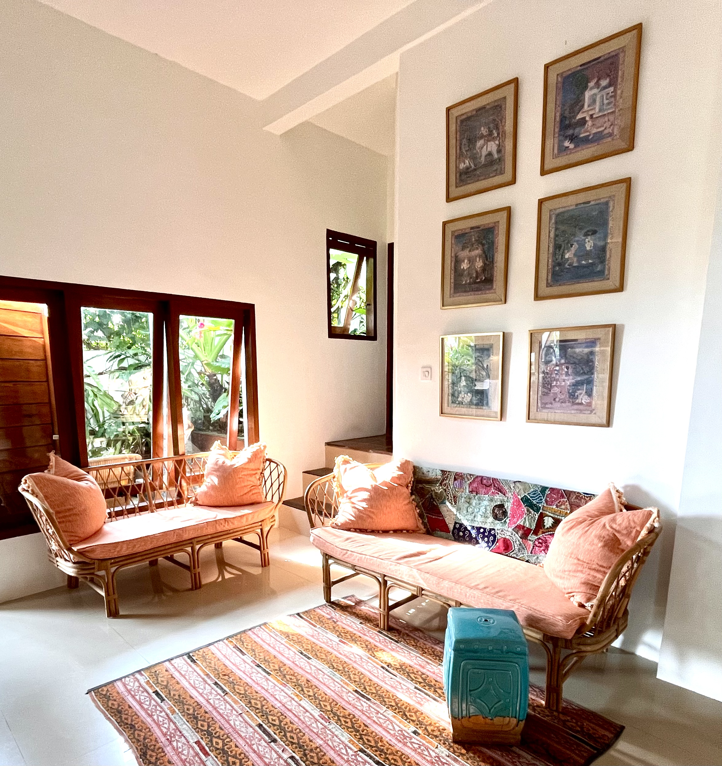 Sunlit living room with rattan furniture, couture fabrics, colorful wall art, and a patterned rug.