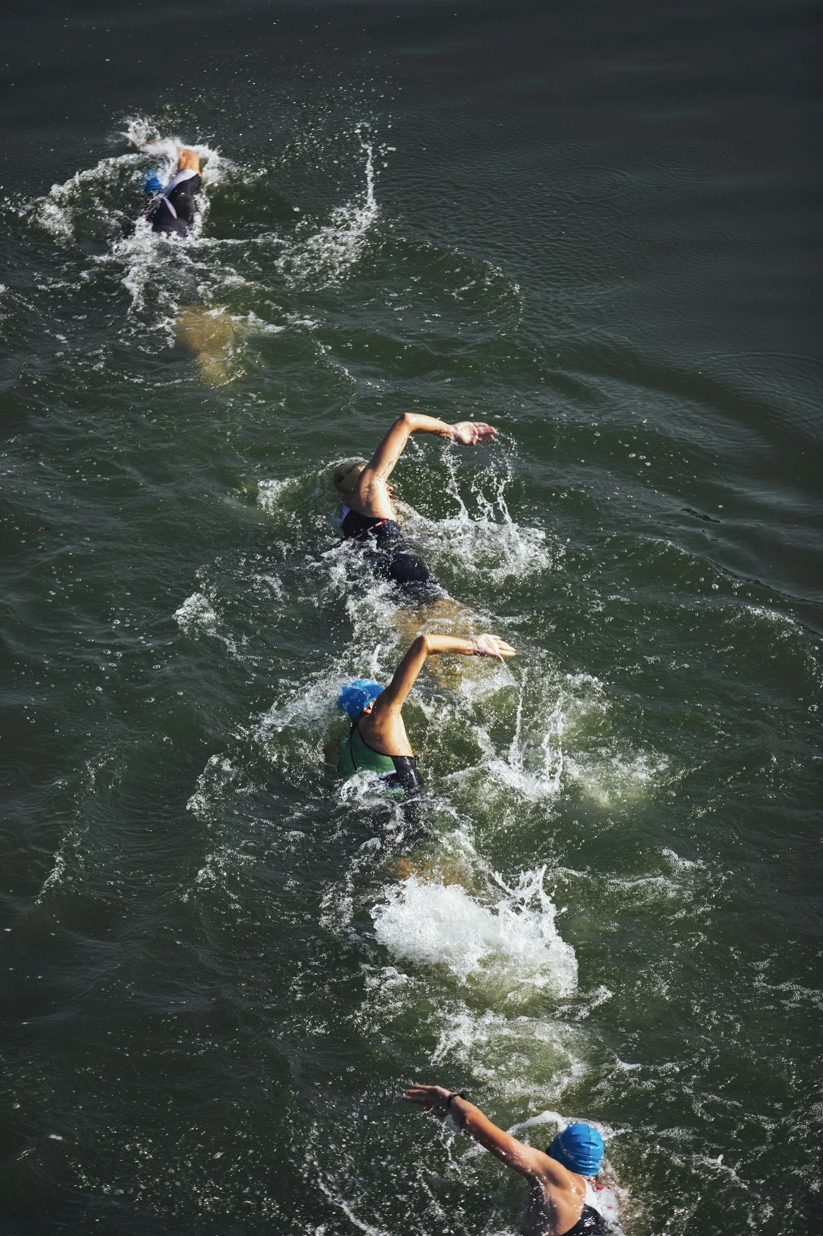 Four swimmers wearing helmets and swimsuits swimming in open water during a race.