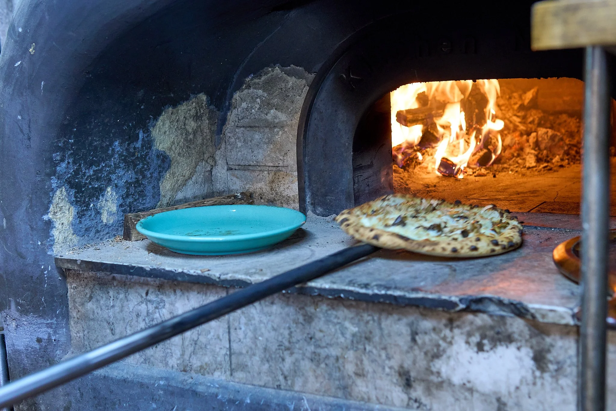 窯で焼かれているピザと空の青い皿
