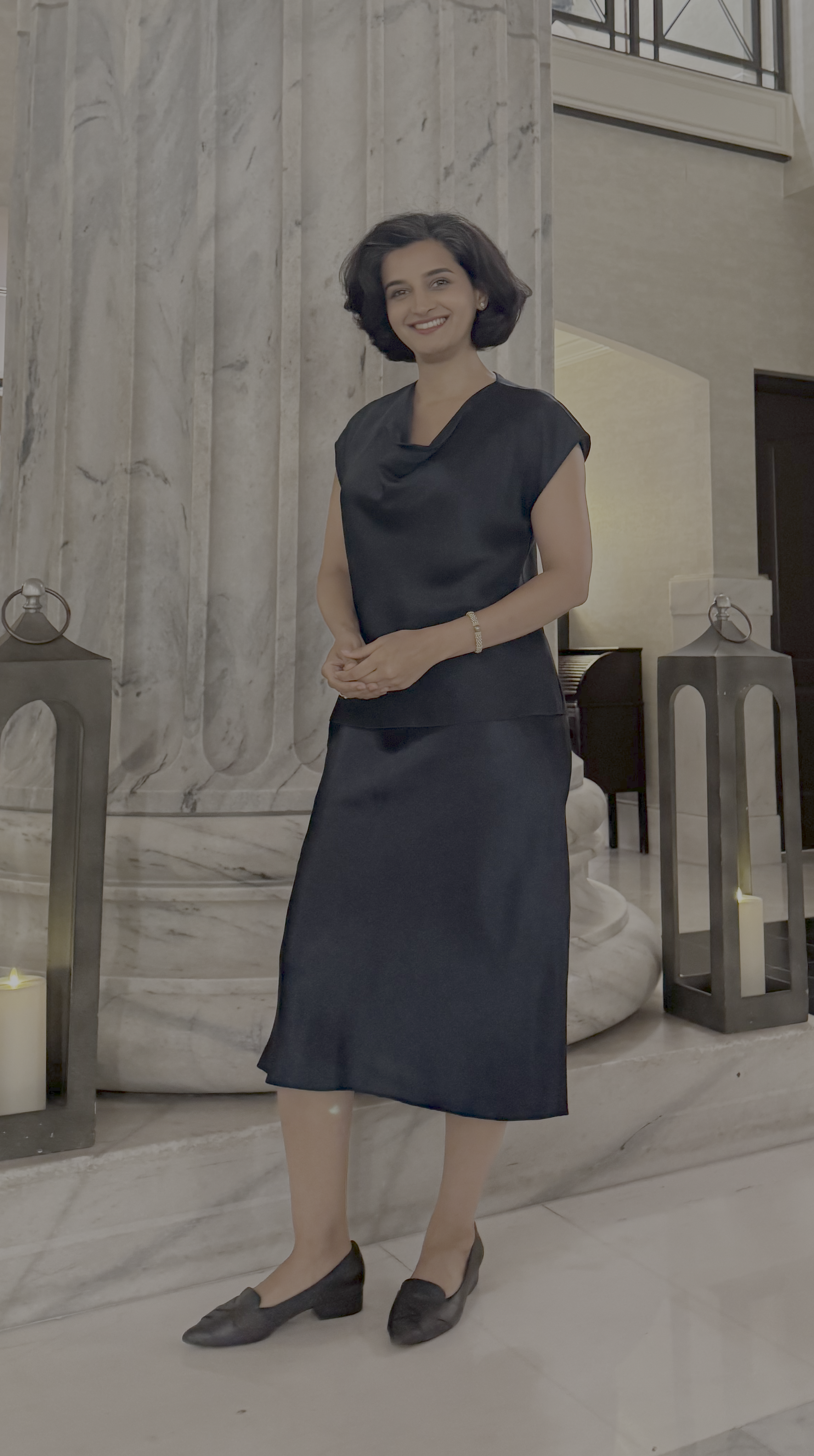 A woman in a black dress standing inside a building with marble columns and soft lighting.