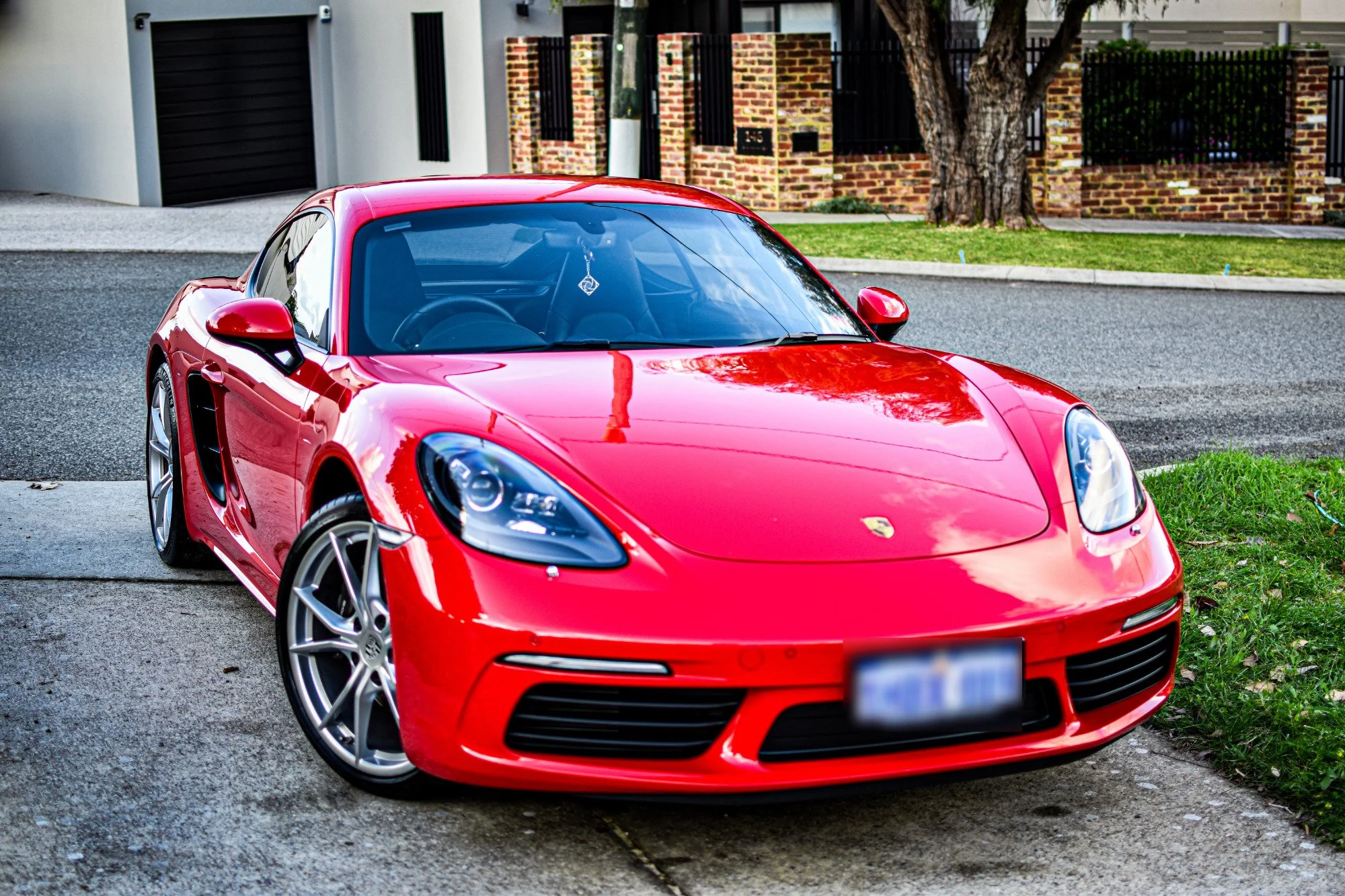Red Porsche sports car parked on a driveway in front of a residential building with brick walls and a tree.