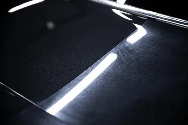Close-up of a black car with reflective paint and bright overhead lighting