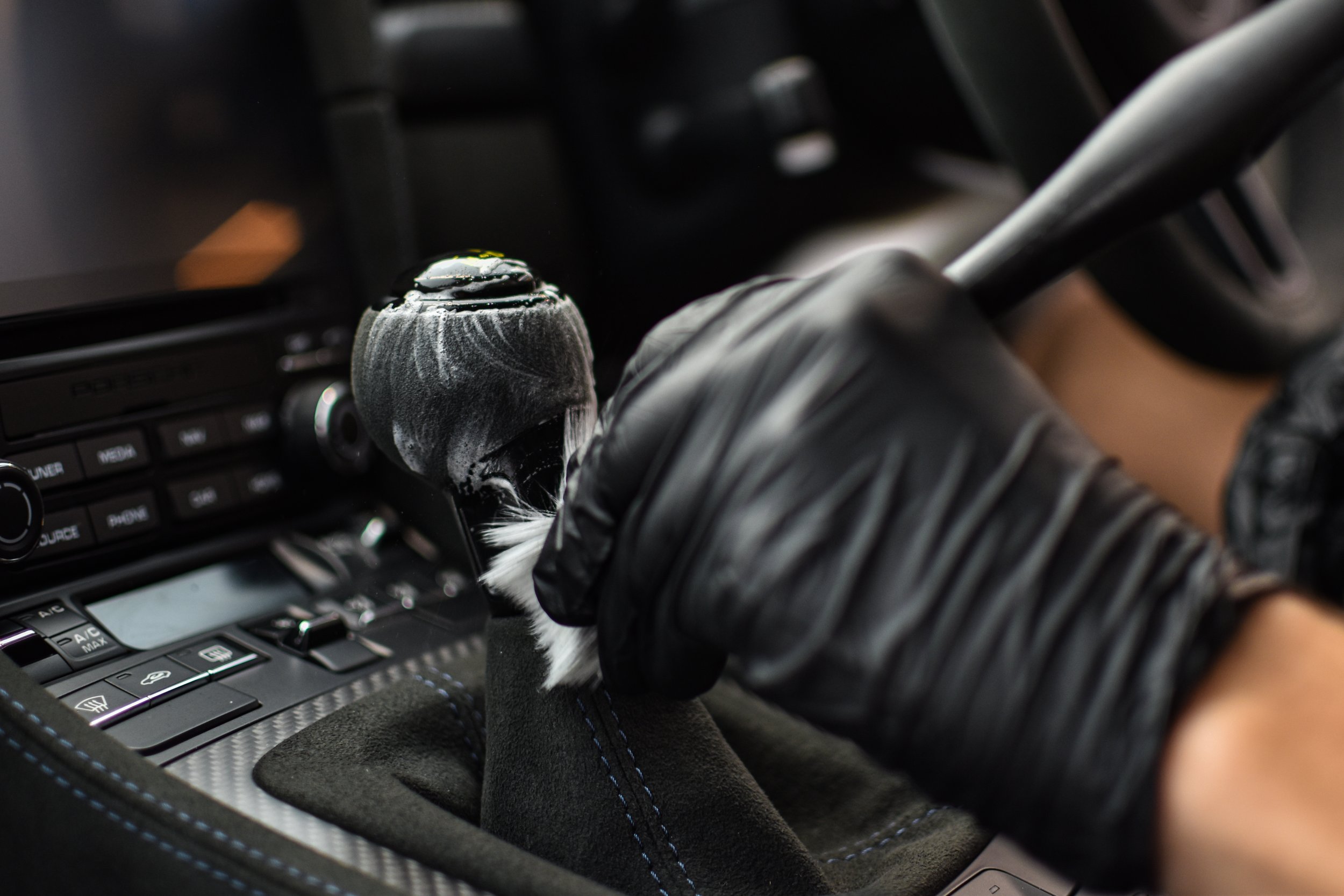 Close-up of a person's gloved hand shifting a gear stick in a car, with the car's center console visible.