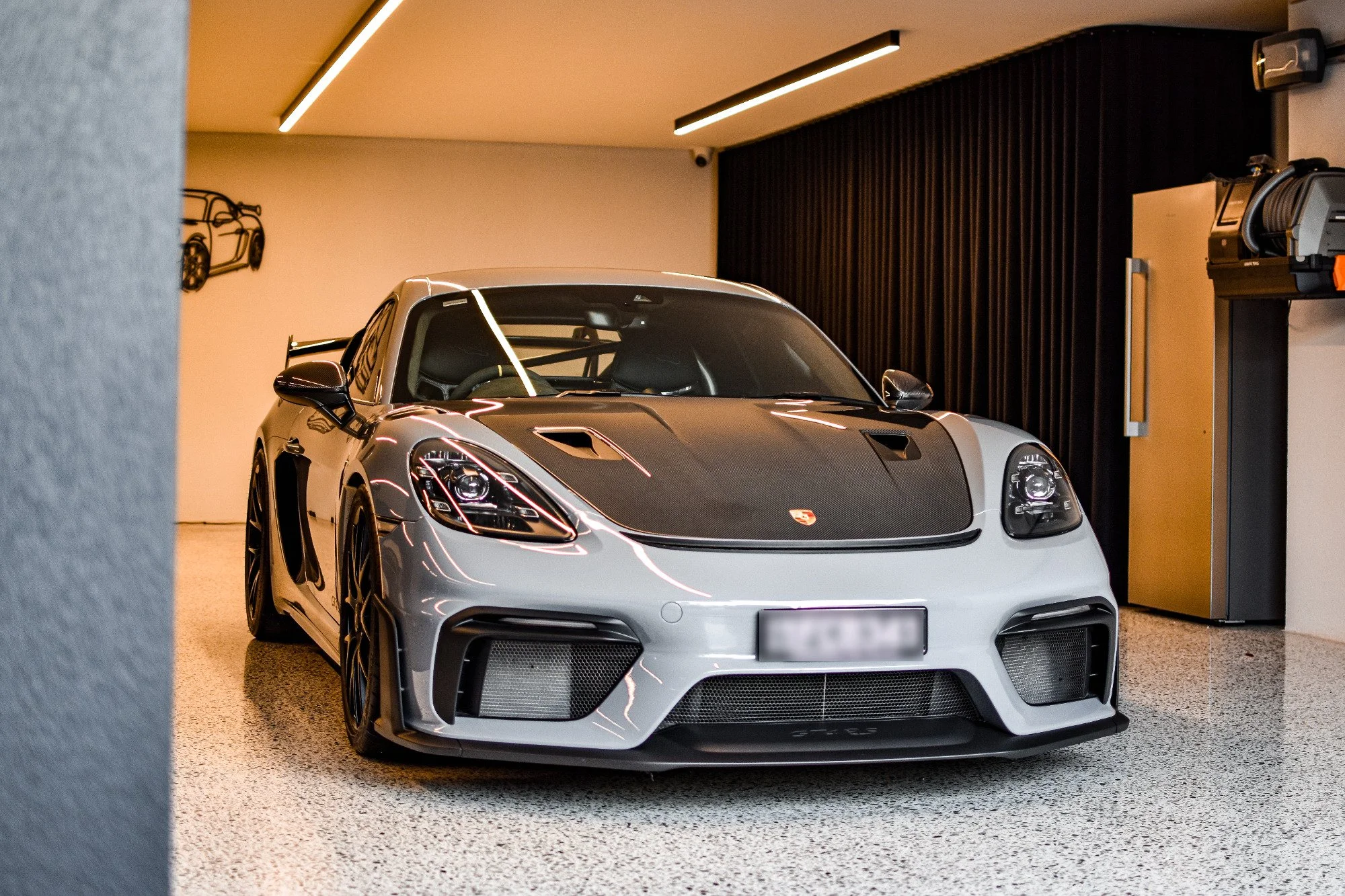 A silver high-performance sports car parked indoors, featuring a black carbon fiber hood and aggressive front design.