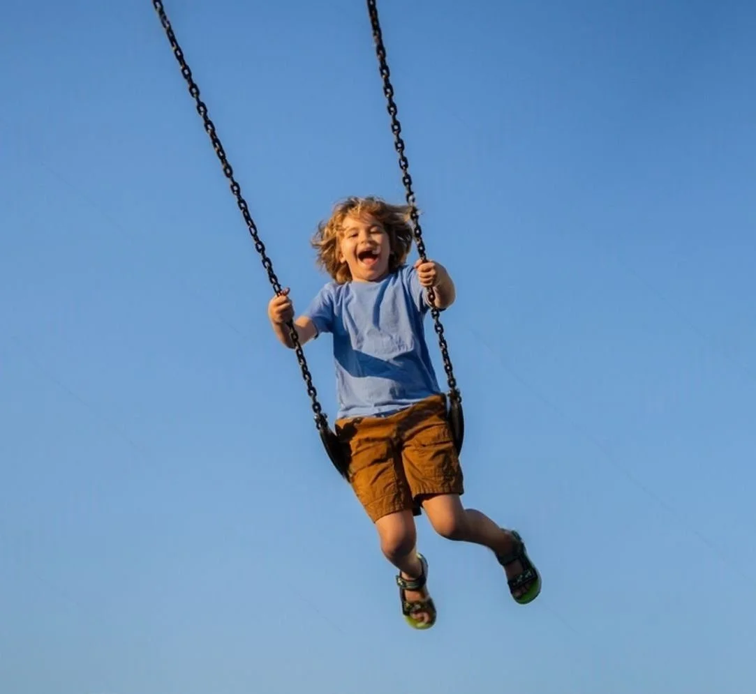 Niño feliz en un columpio suspendido en el aire bajo un cielo azul.
