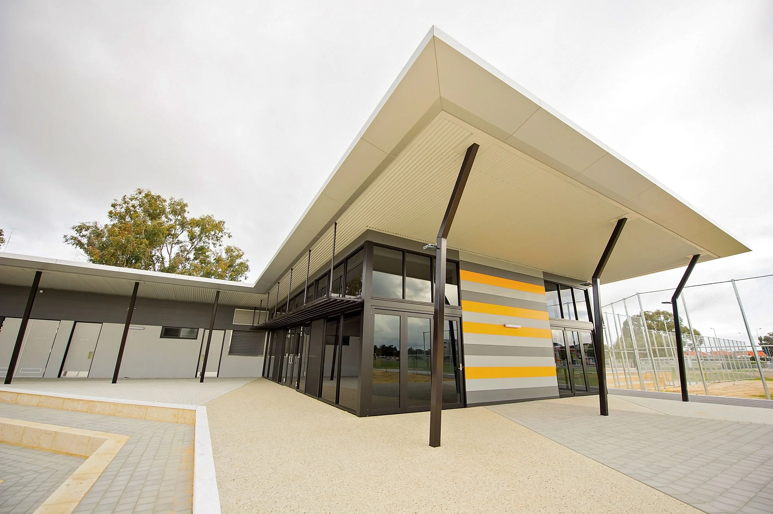 Modern sports facility building with large overhanging roof, glass walls, and adjacent outdoor tennis courts.