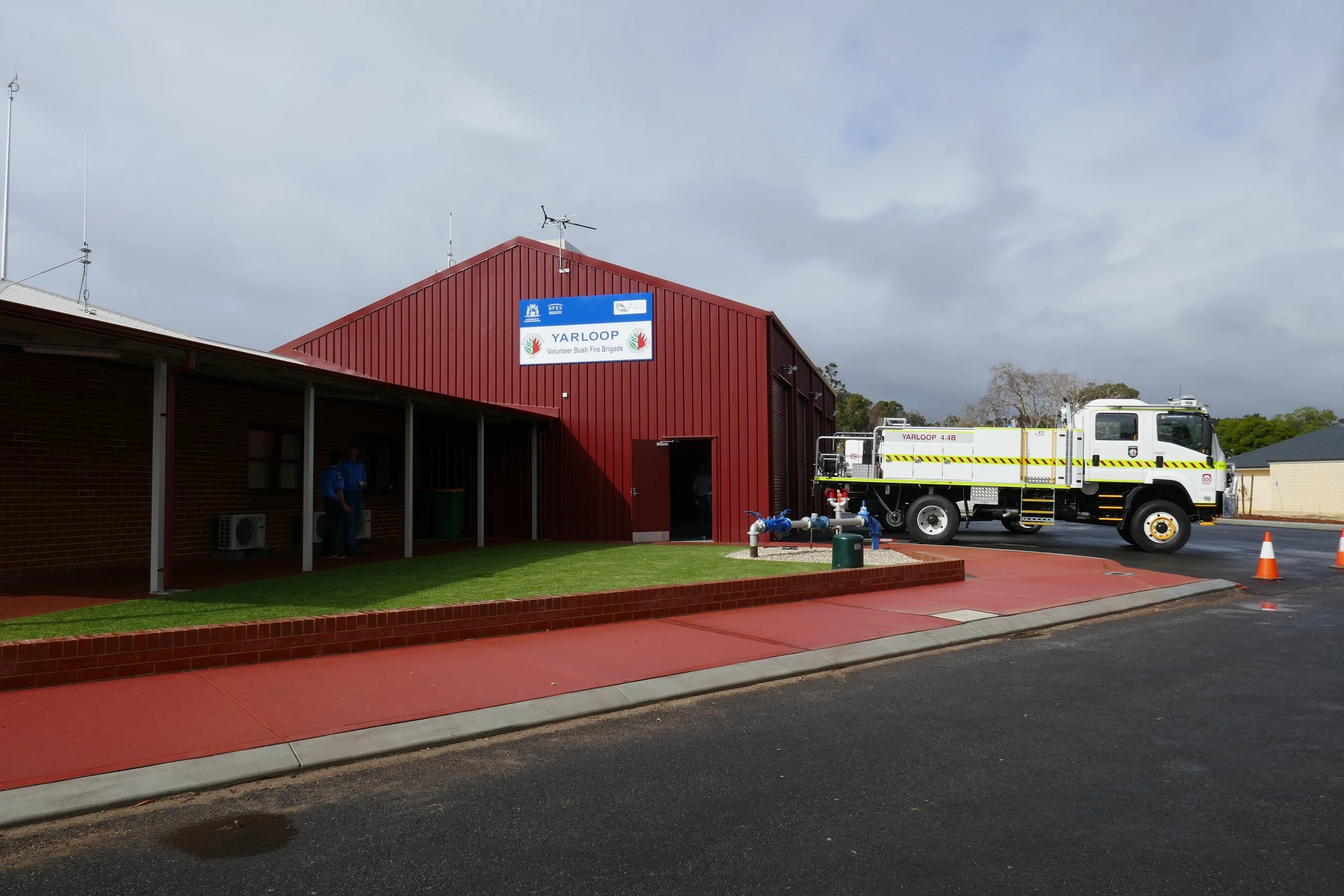 Fire truck parked outside a red community hall with a sign reading YARLOOP Volunteer Bush Fire Brigade, under cloudy sky.