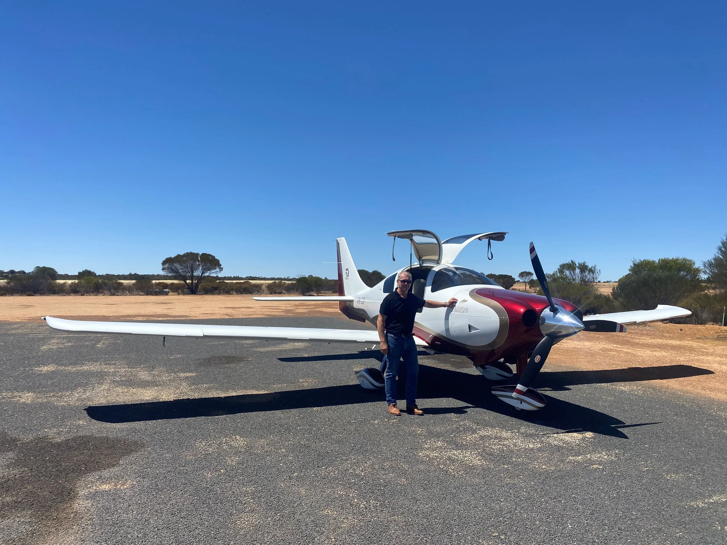 Man standing next to small private plane on an outback runway with some trees in the background