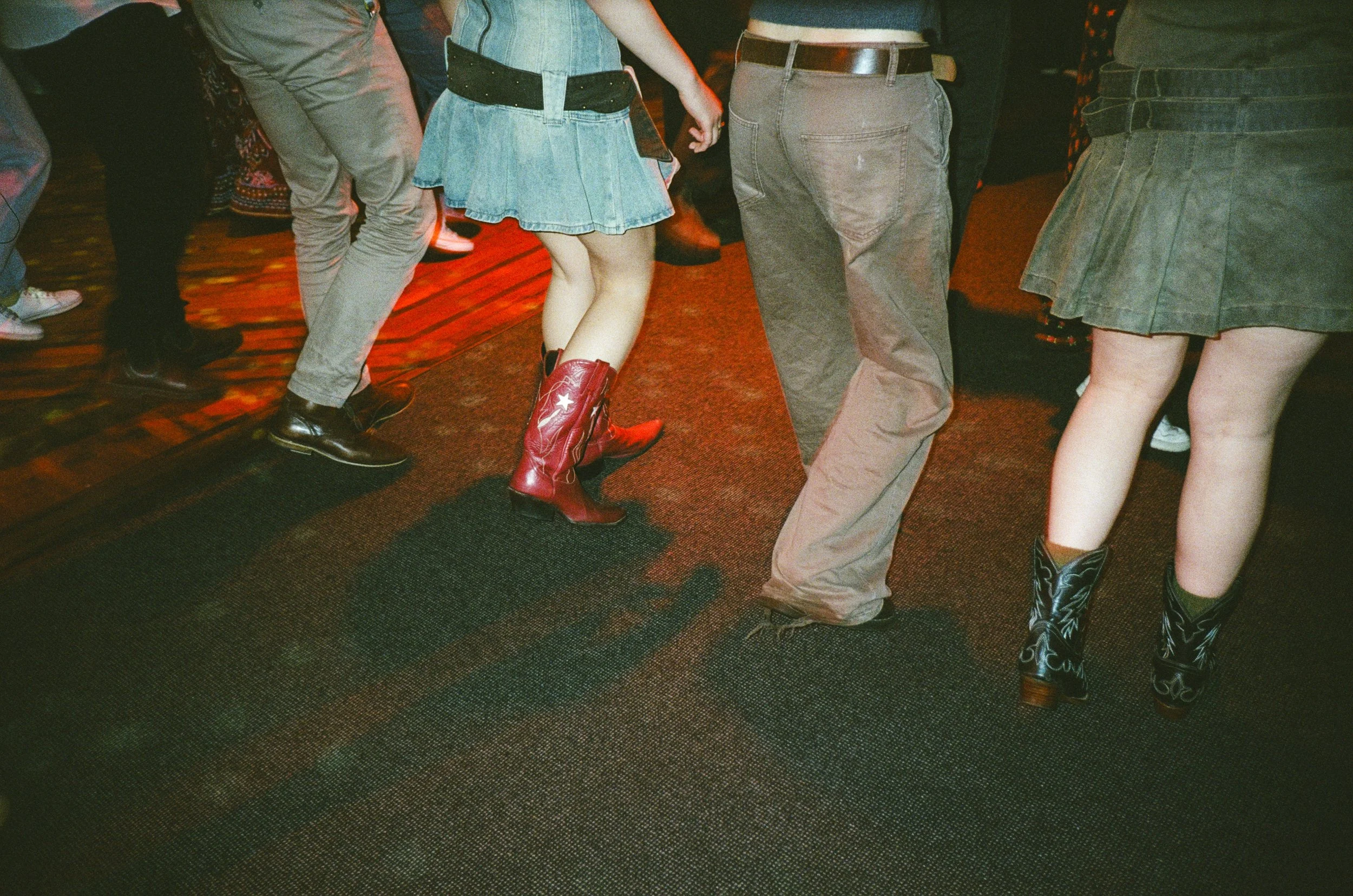 People dancing in cowboy boots on a dimly lit dance floor.
