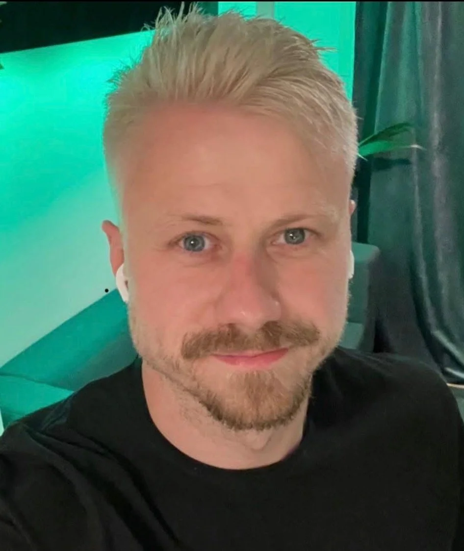 en man med ljus hårt, kort skägg och mustasch tittar in i kameran framför en grön bakgrund