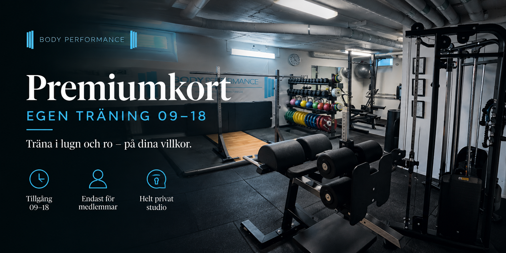 En träningsstudio med olika vikter och träningsutrustning, inredd med svart mattgolv och industribyggnadsdetaljer.