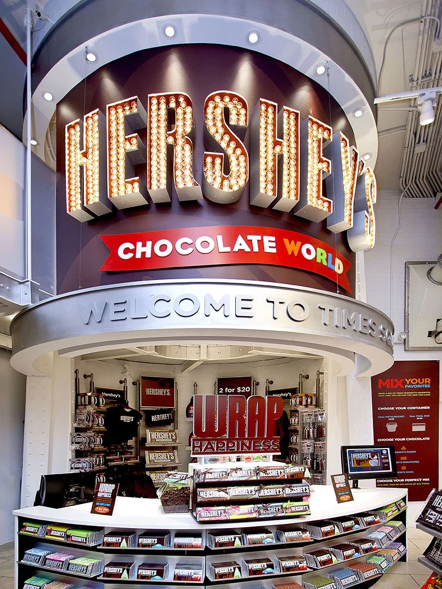 Hershey's Chocolate World store at Times Square with a large illuminated sign and a cashier counter, featuring Hershey's chocolate products and signage.
