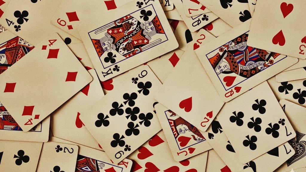 A scattered pile of playing cards, including hearts, diamonds, clubs, and spades, with some cards face up showing various numbers and face cards.