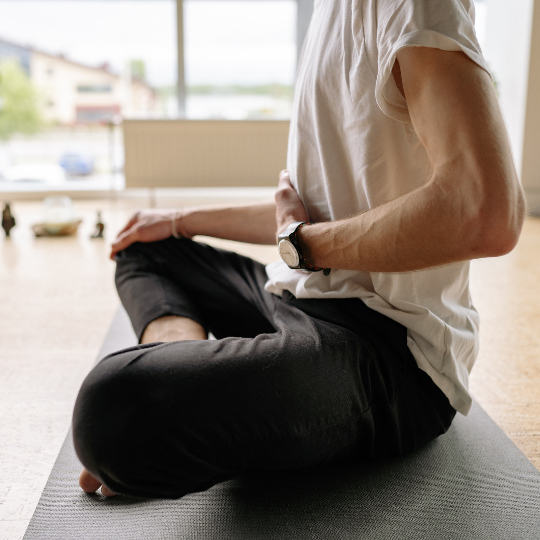 Person practicing yoga or meditation indoors, sitting cross-legged on a mat near a window.