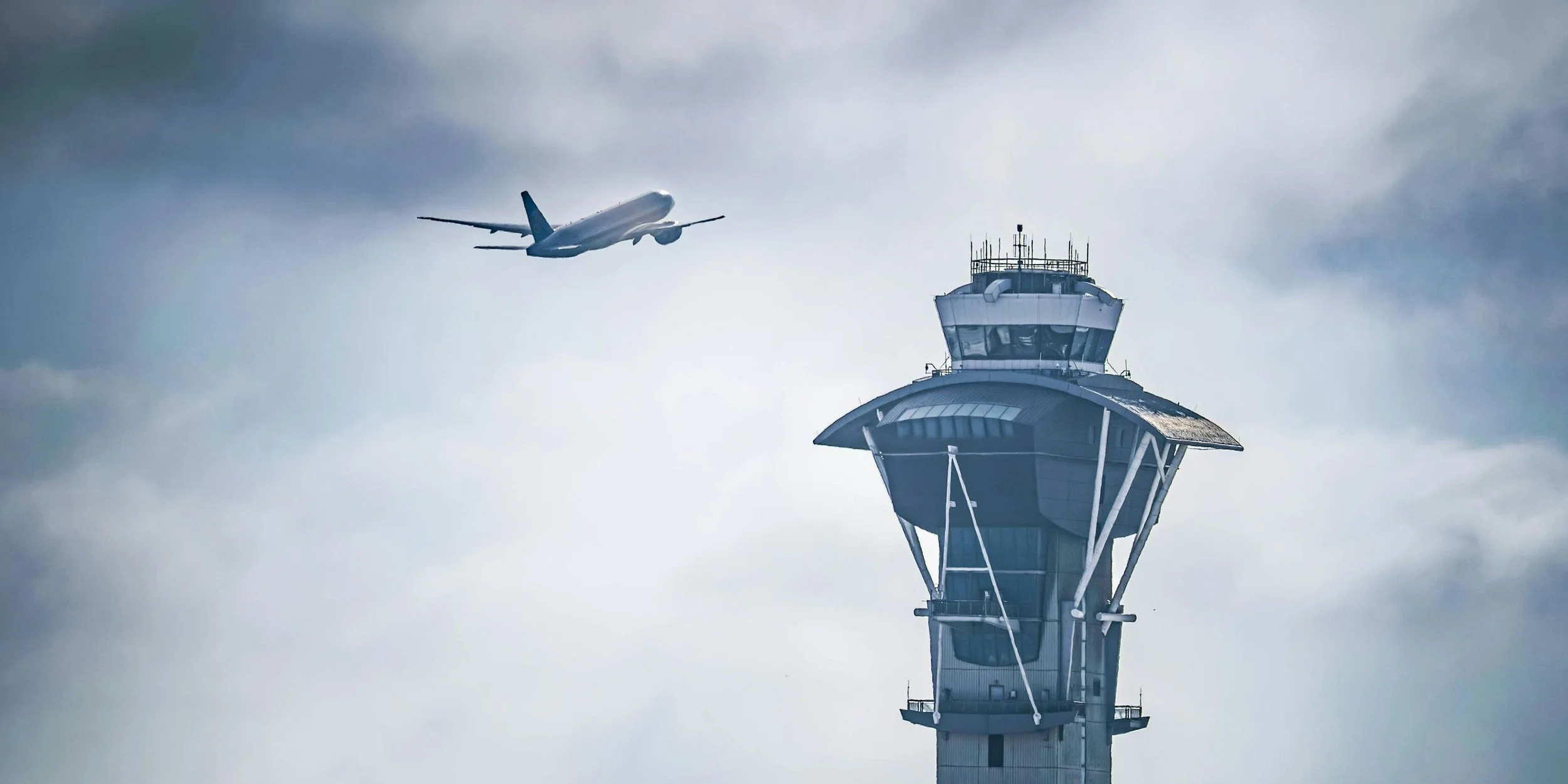 An airplane flying near an airport control tower on a cloudy day.