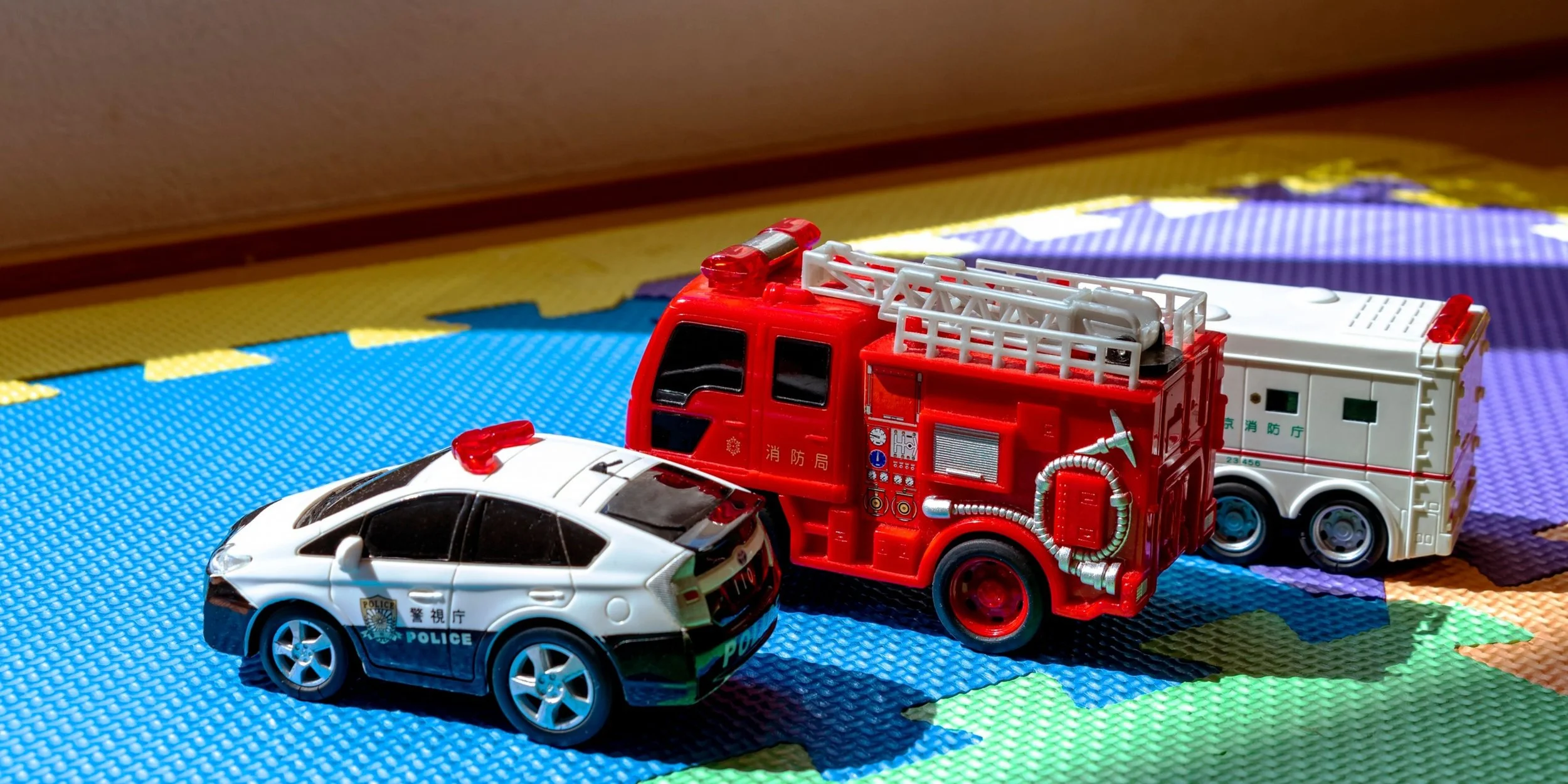 Toy police car, fire truck, and ambulance placed on a colorful foam play mat.