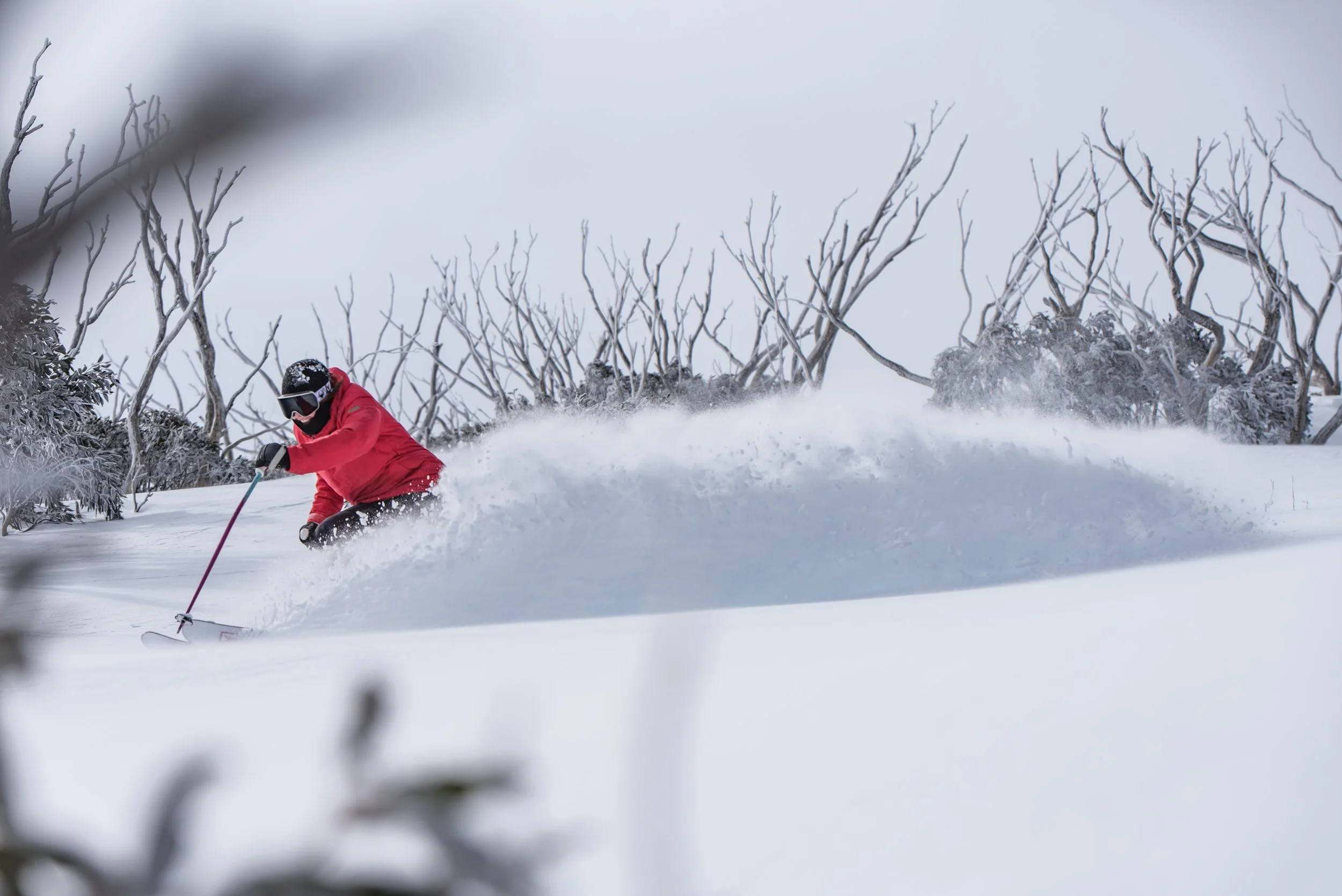 Skier in a red jacket slashing powder at Hotham ski resort