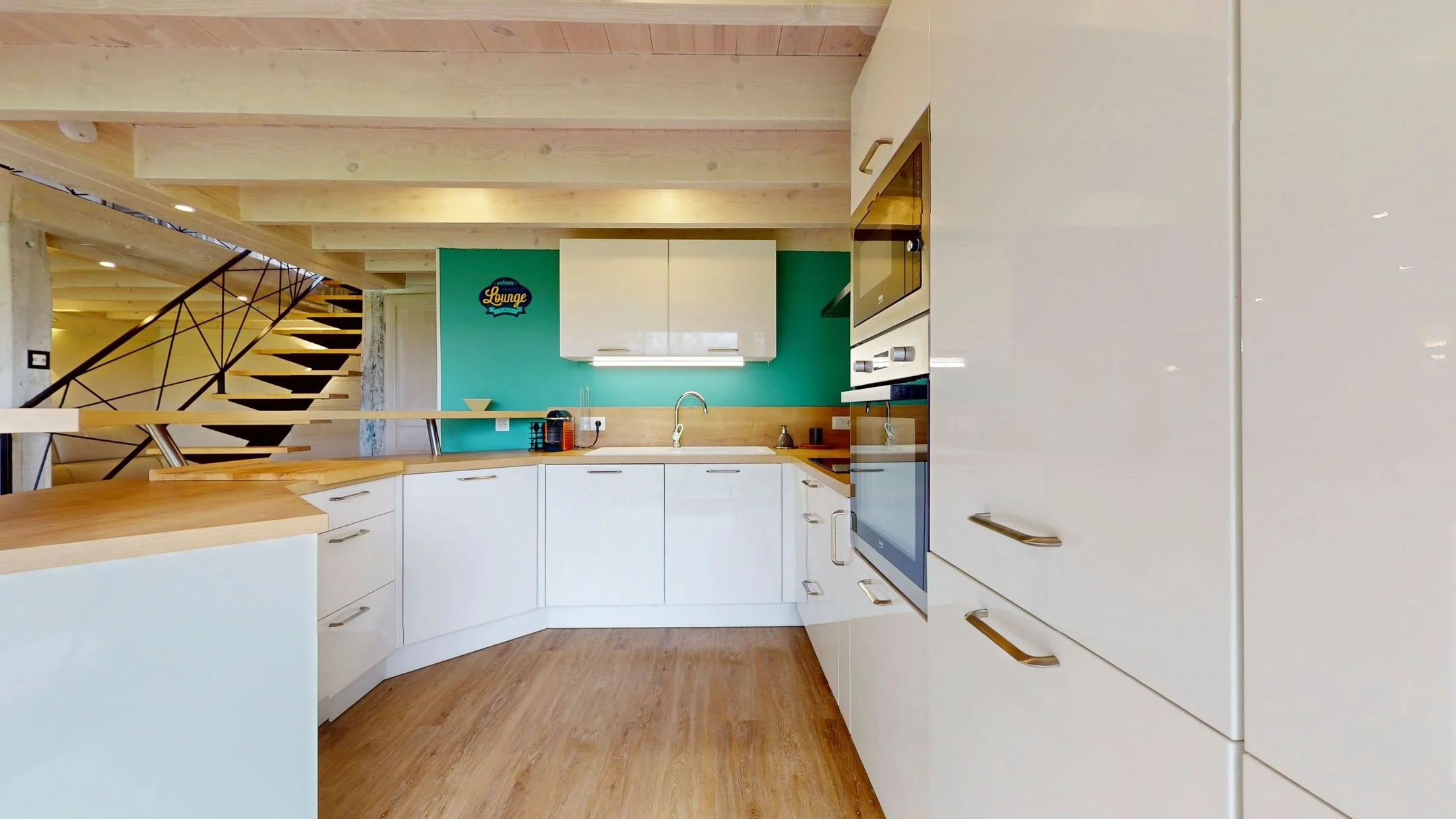 Cuisine moderne avec armoires blanches, plan de travail en bois, mur turquoise, et appareils électroménagers intégrés.