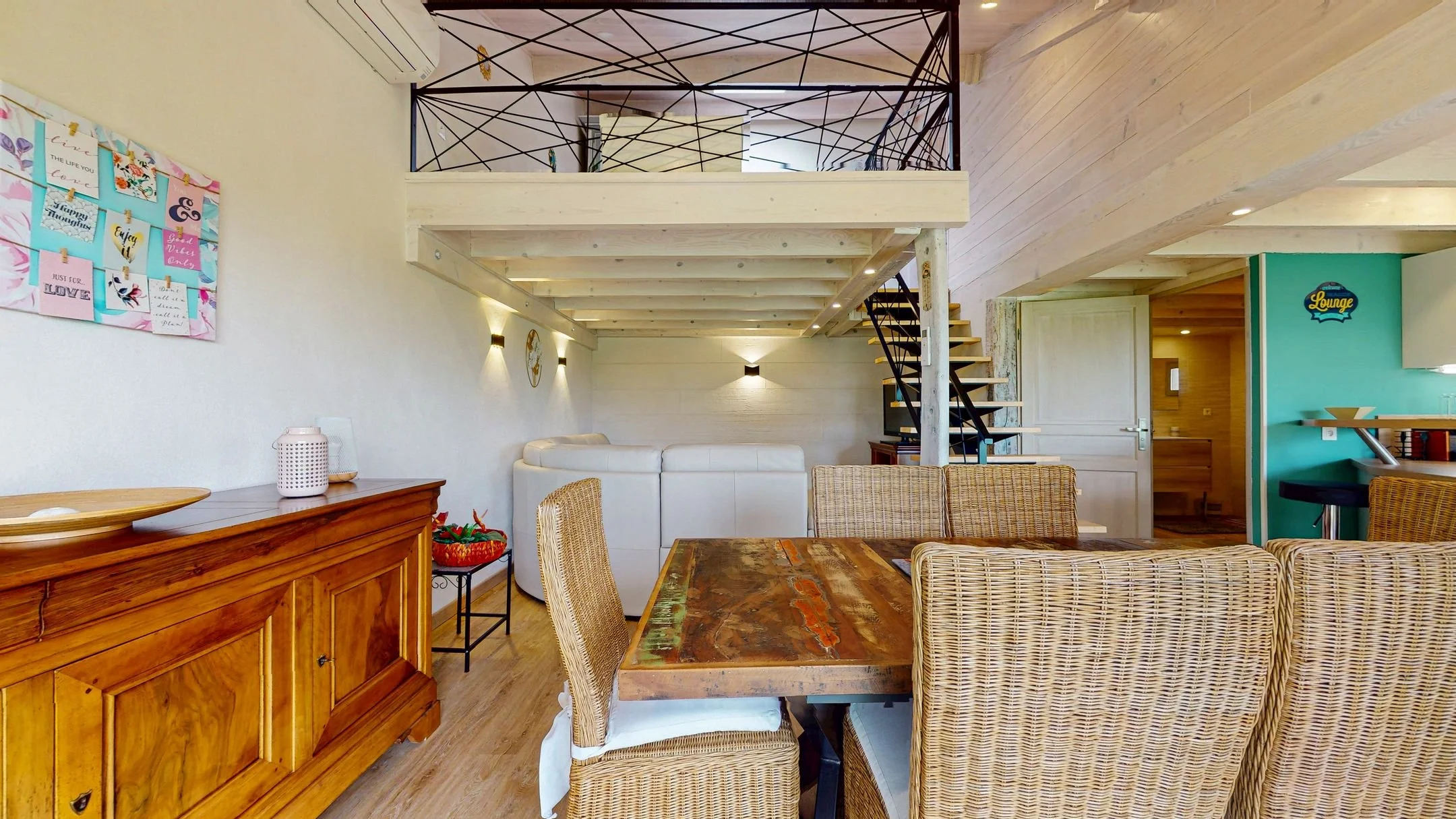 Intérieur d'une pièce avec un espace repas, un canapé blanc, une mezzanine avec une balustrade en métal noir, un escalier en spirale en bois et métal, murs beige, décoration moderne et bois clair.