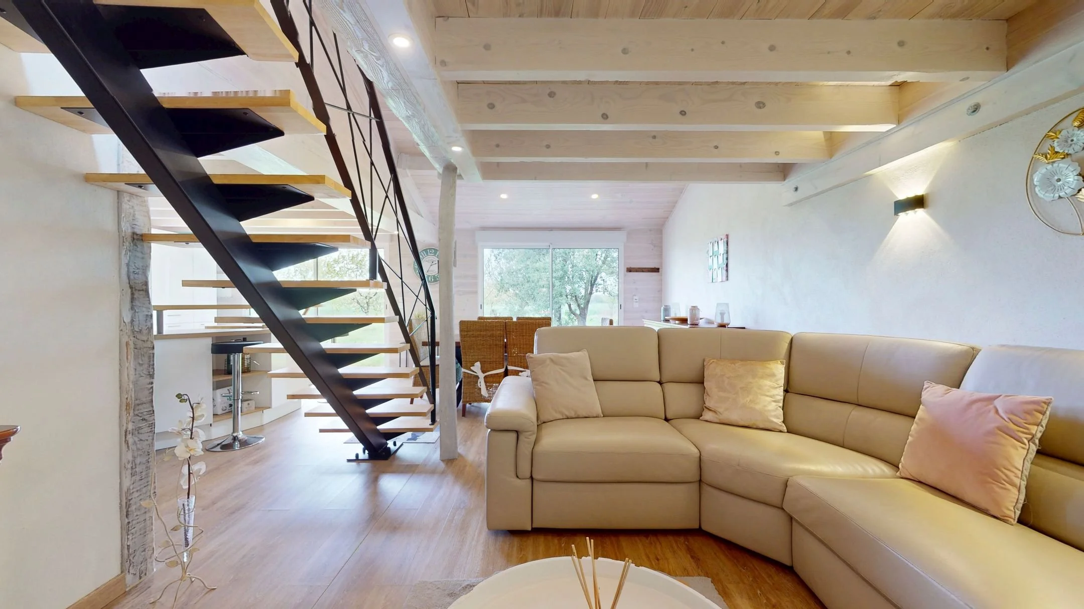 Salon lumineux avec canapé beige, escalier en bois et métal, grande fenêtre, décoration moderne.