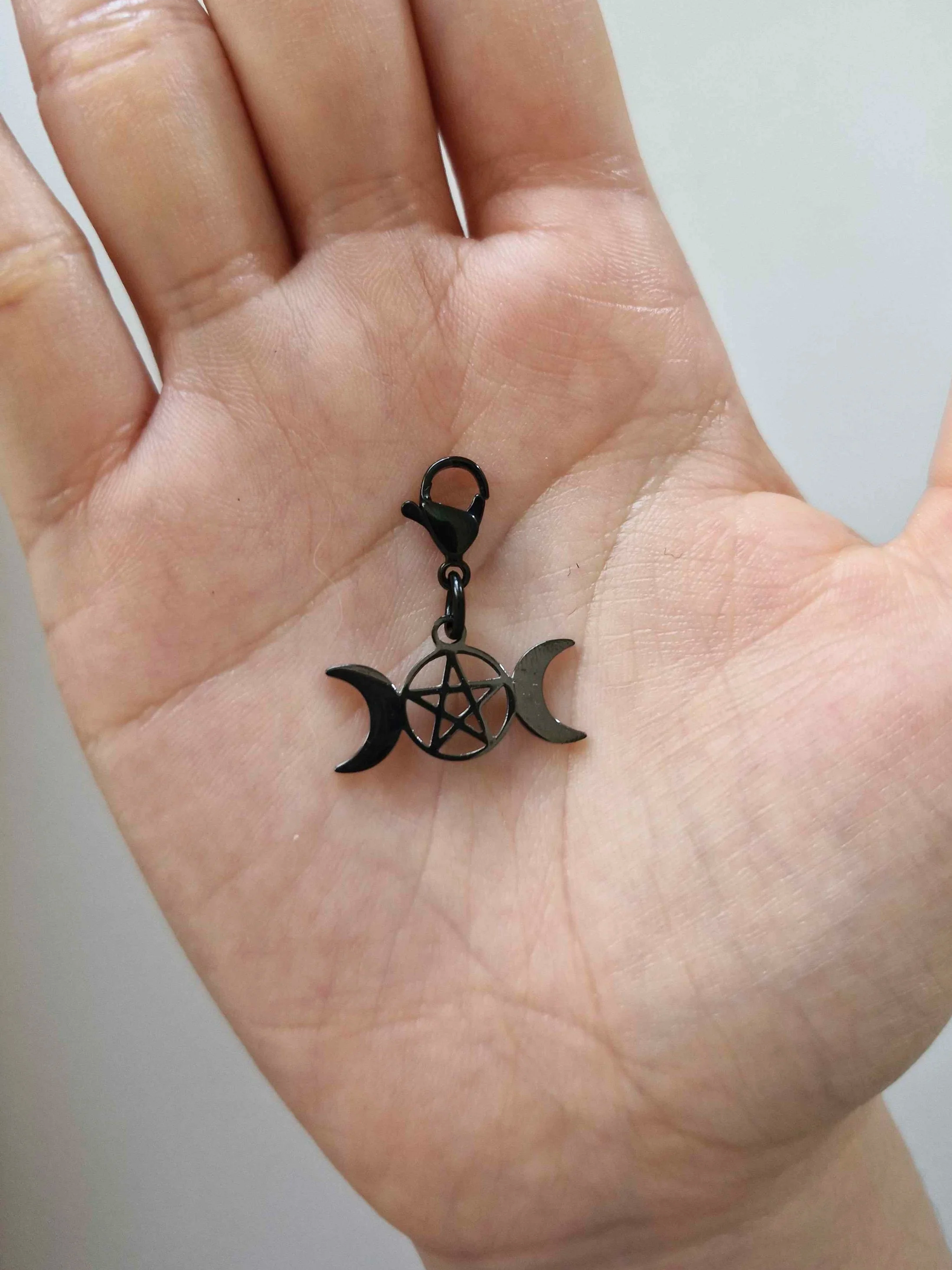 Black stainless-steel triple moon pentacle charm resting on a hand to show scale | Celestia’s Charms