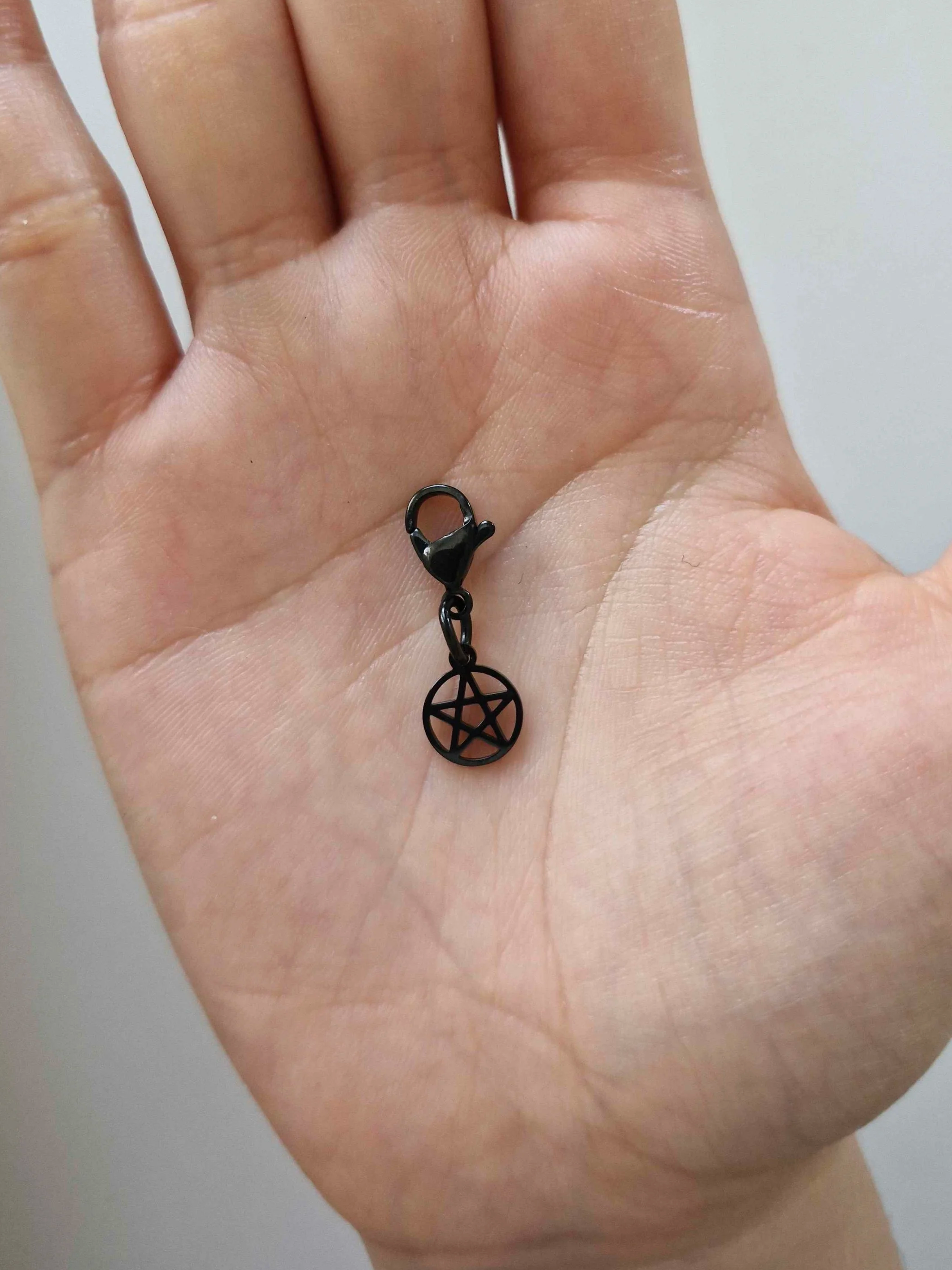 Black stainless-steel mini pentagram charm resting on a hand to show scale | Celestia’s Charms