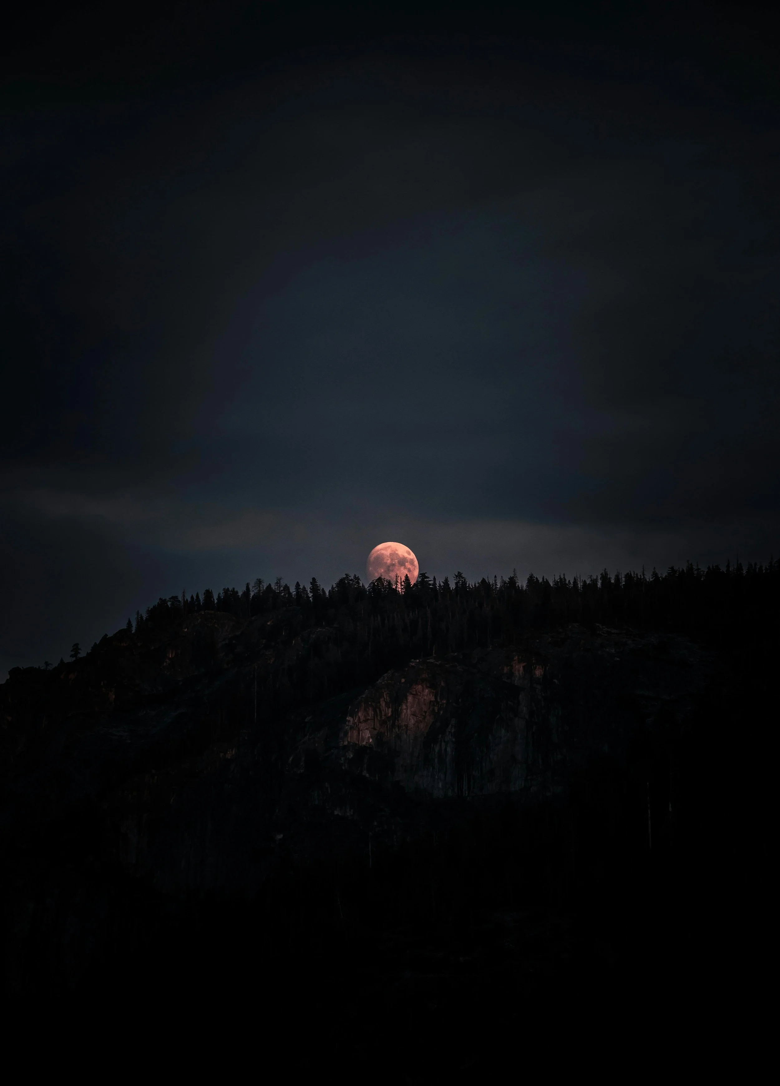 Full moon rising above a dark mountain silhouette with a cloudy night sky.