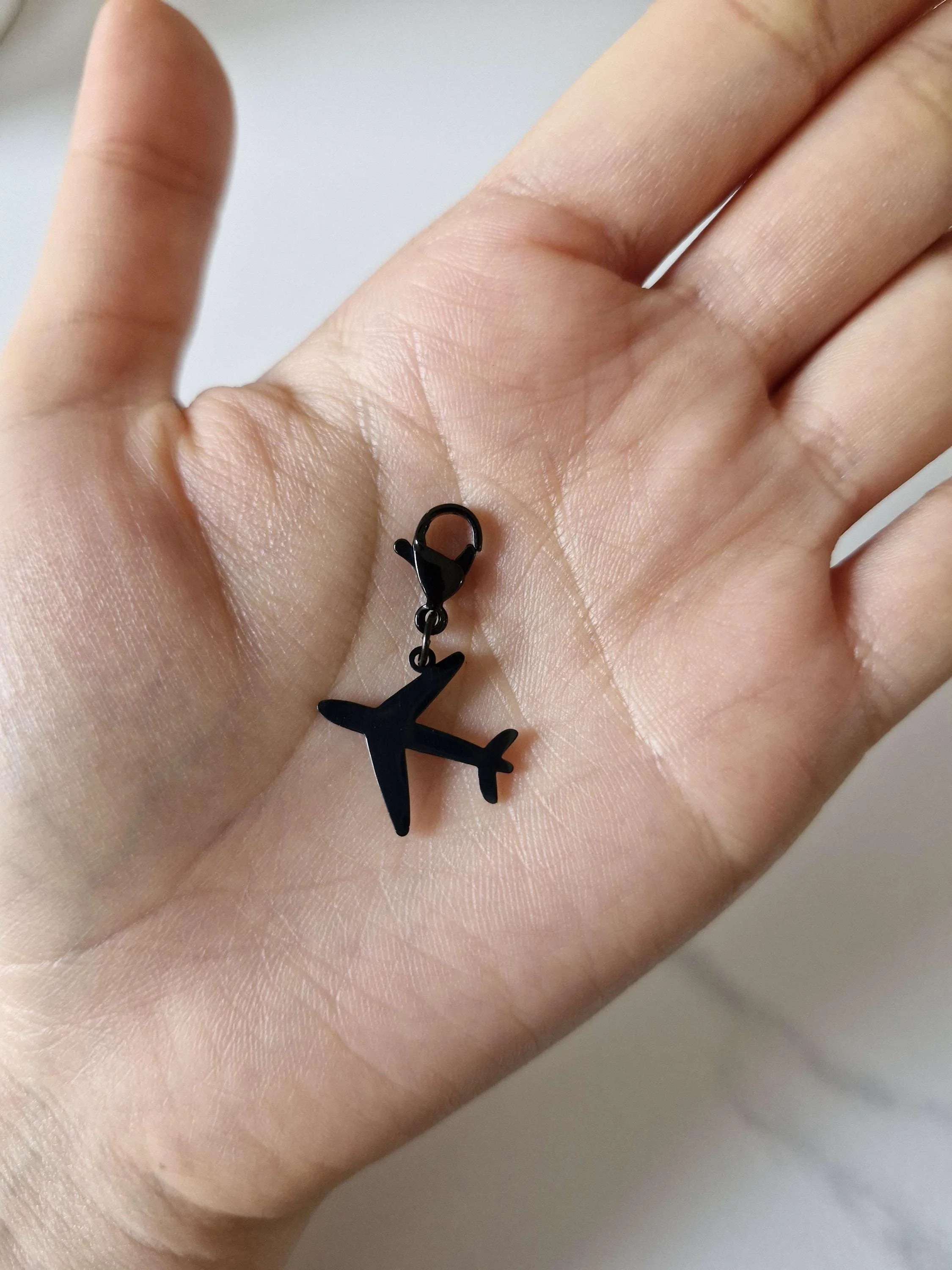 Black stainless-steel airplane charm resting on a hand to show scale | Celestia’s Charms