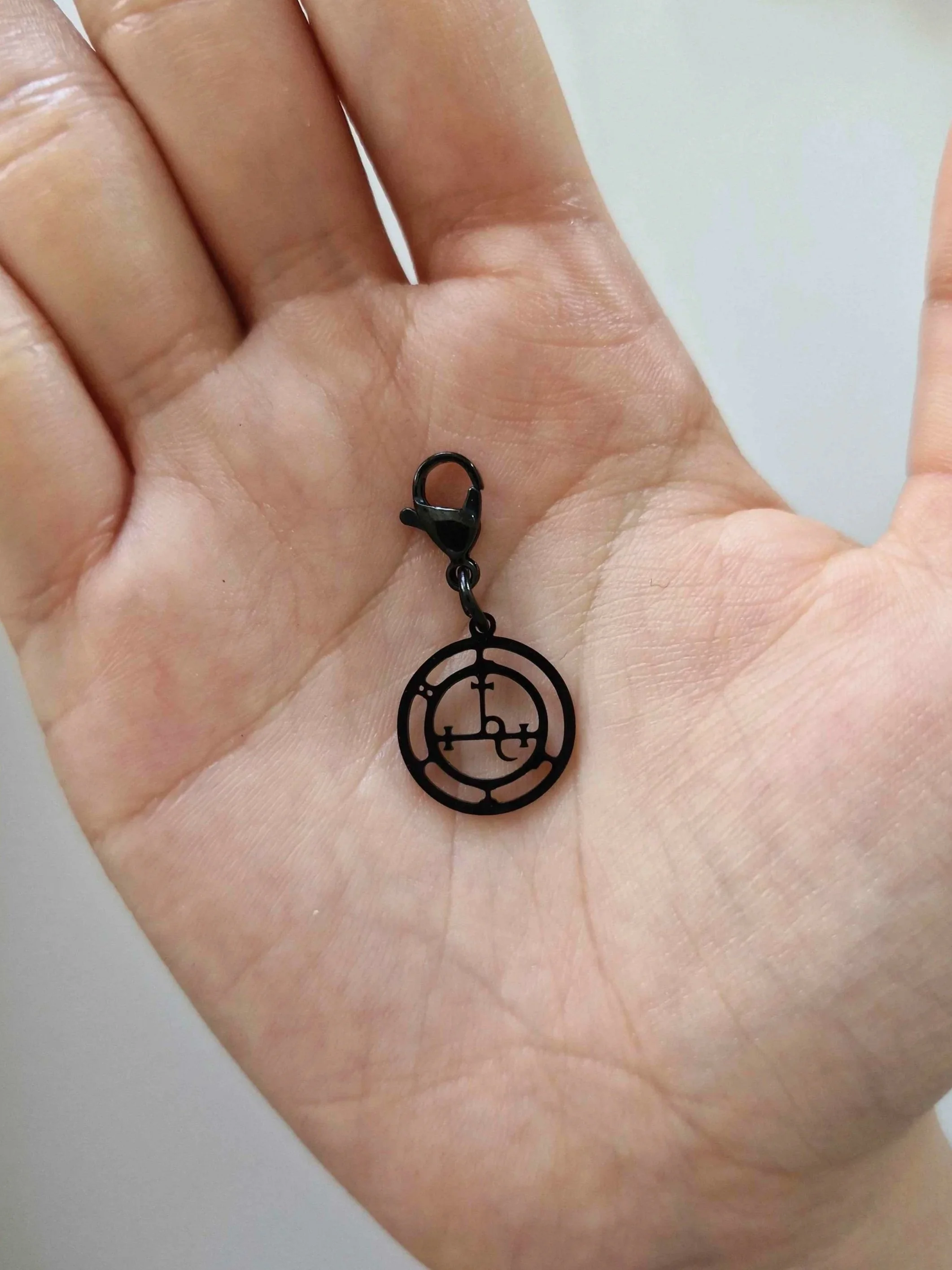 Black stainless-steel sigil of Lilith charm resting on a hand to show scale | Celestia’s Charms