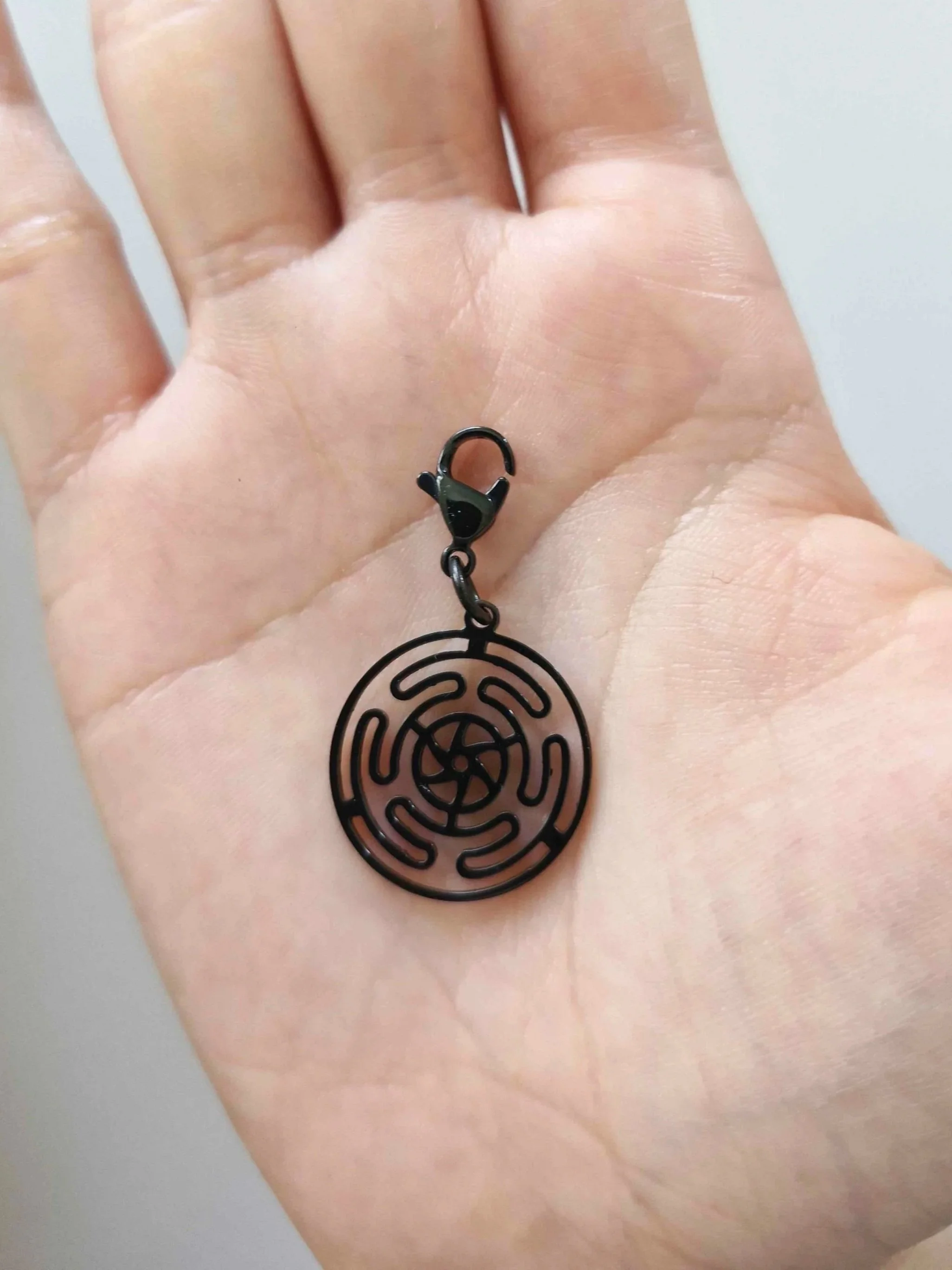 Black stainless-steel Hecate's wheel charm resting on a hand to show scale | Celestia’s Charms