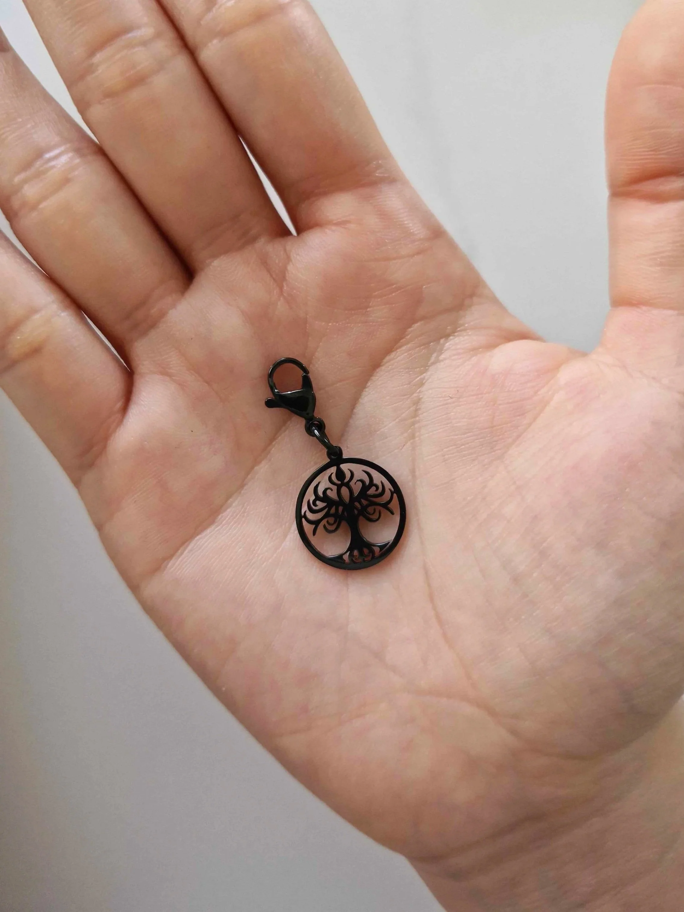 Black stainless-steel tree of life charm resting on a hand to show scale | Celestia’s Charms