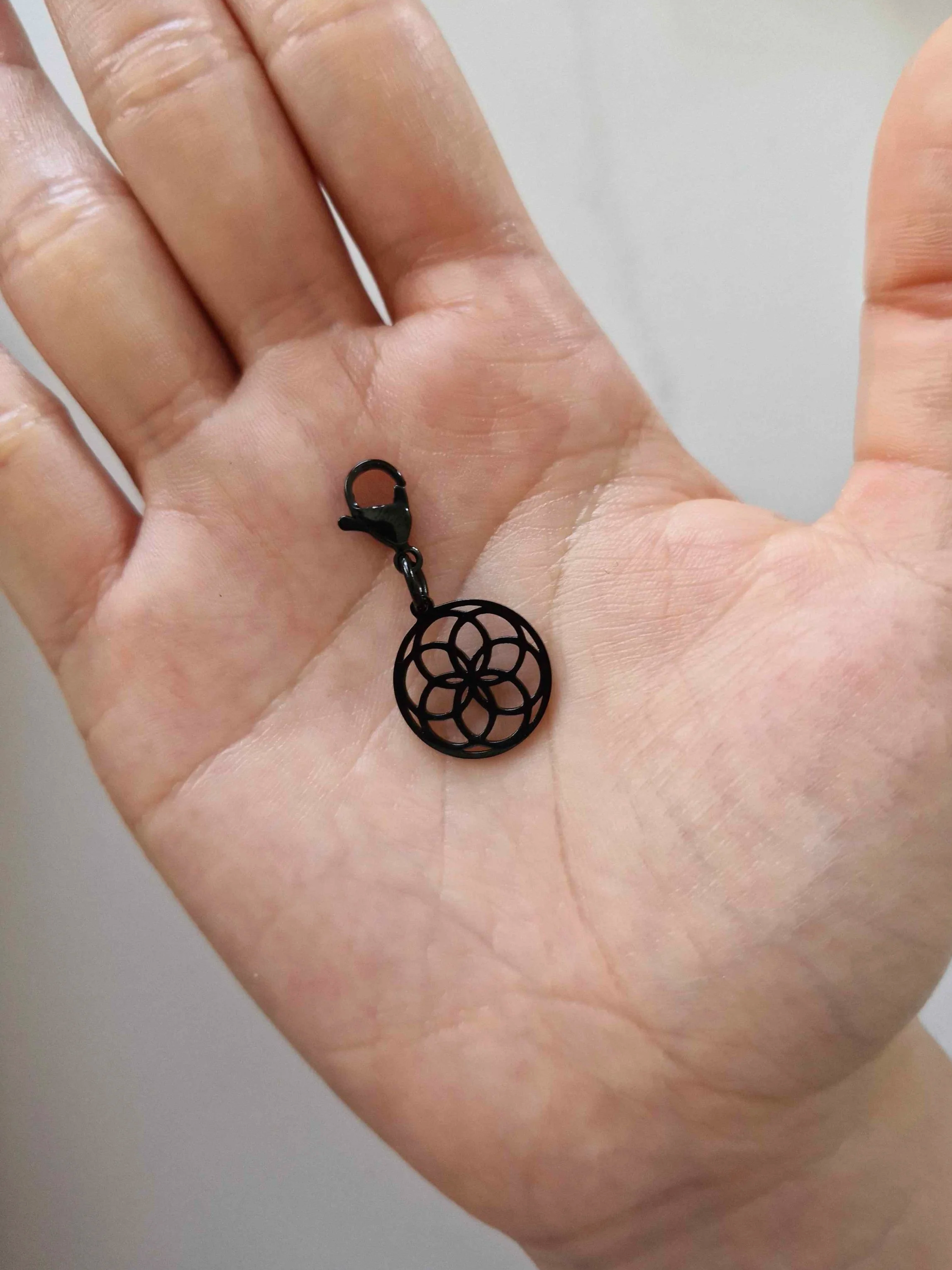 Black stainless-steel seed of life charm resting on a hand to show scale | Celestia’s Charms