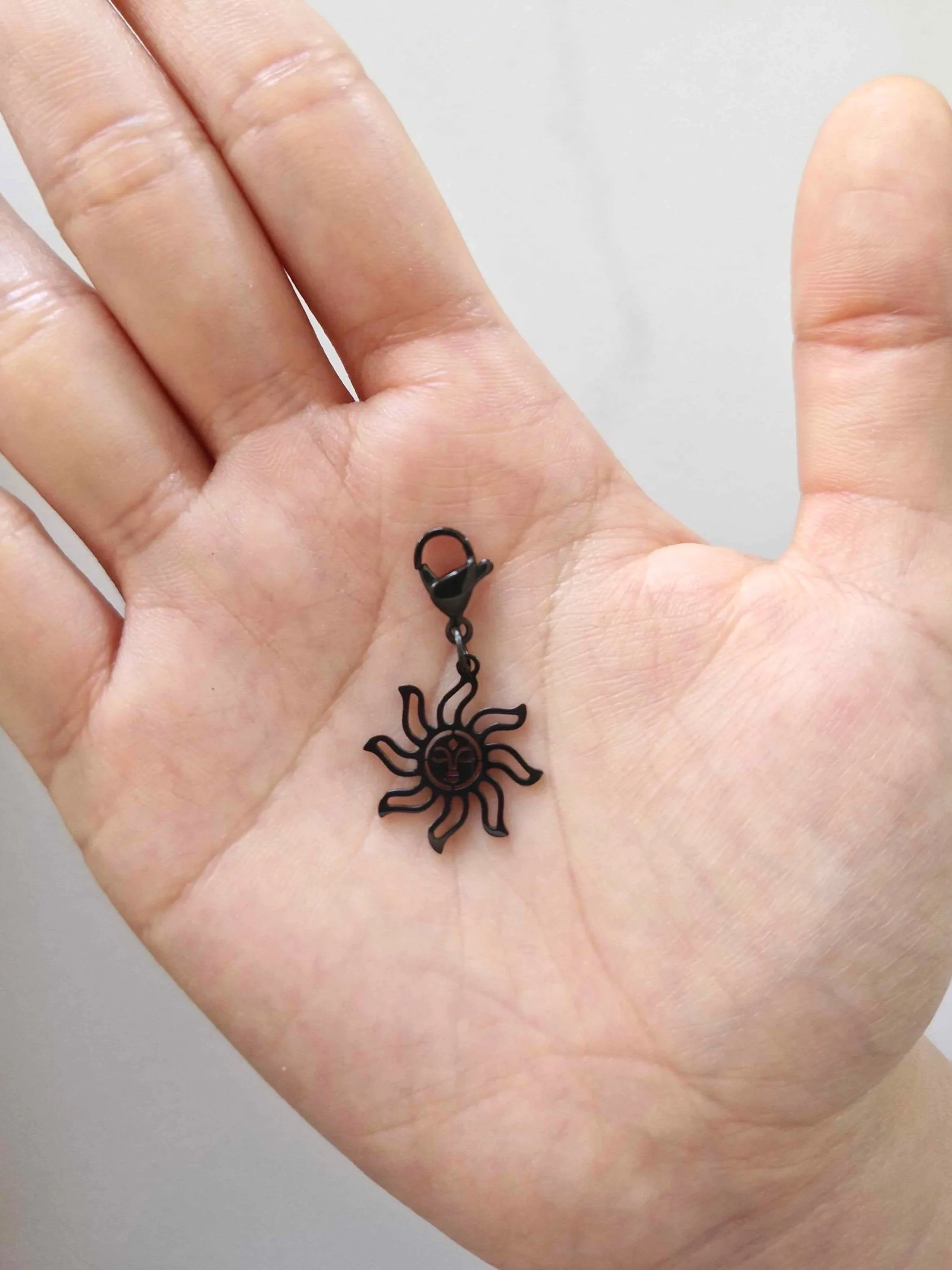 Black stainless-steel sun charm resting on a hand to show scale | Celestia’s Charms
