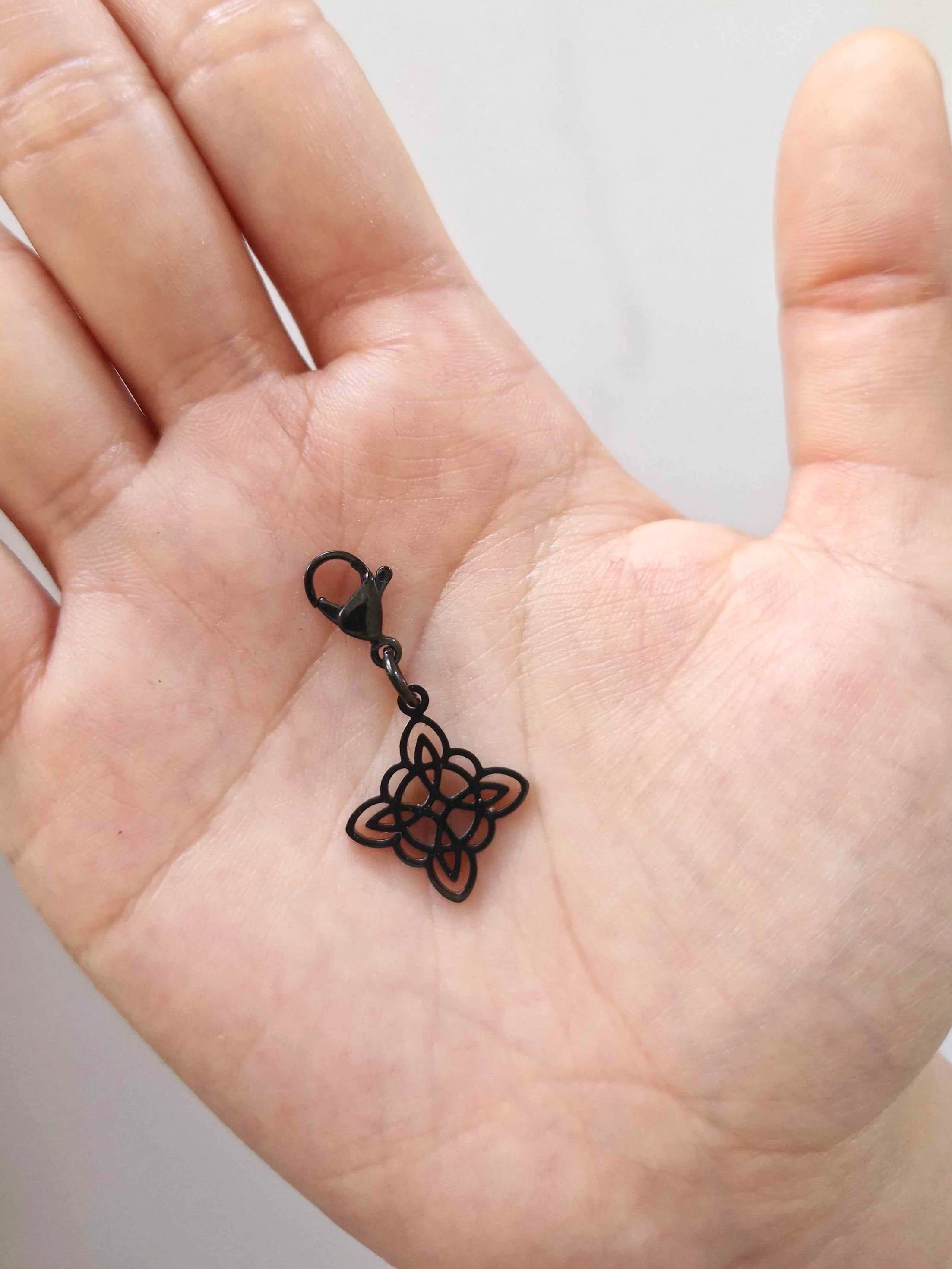 Black stainless-steel witch's knot charm resting on a hand to show scale | Celestia’s Charms
