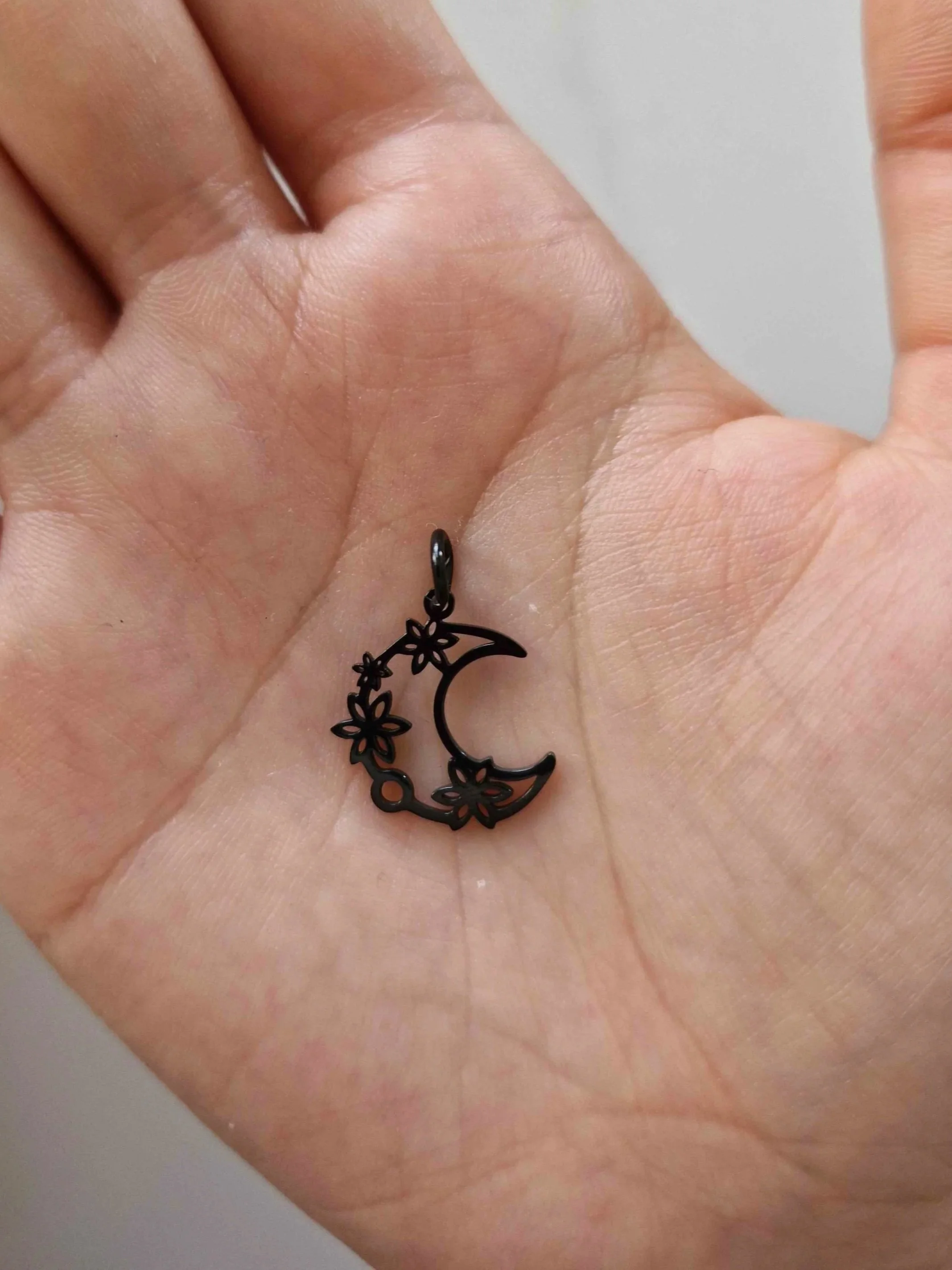 Black stainless-steel moon charm resting on a hand to show scale | Celestia’s Charms.