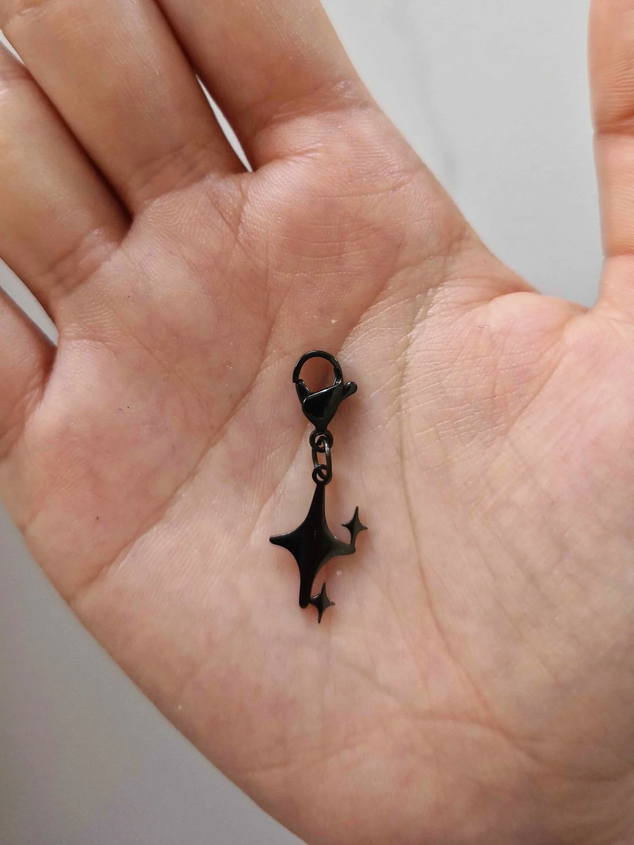 Black stainless-steel stars charm resting on a hand to show scale | Celestia’s Charms.