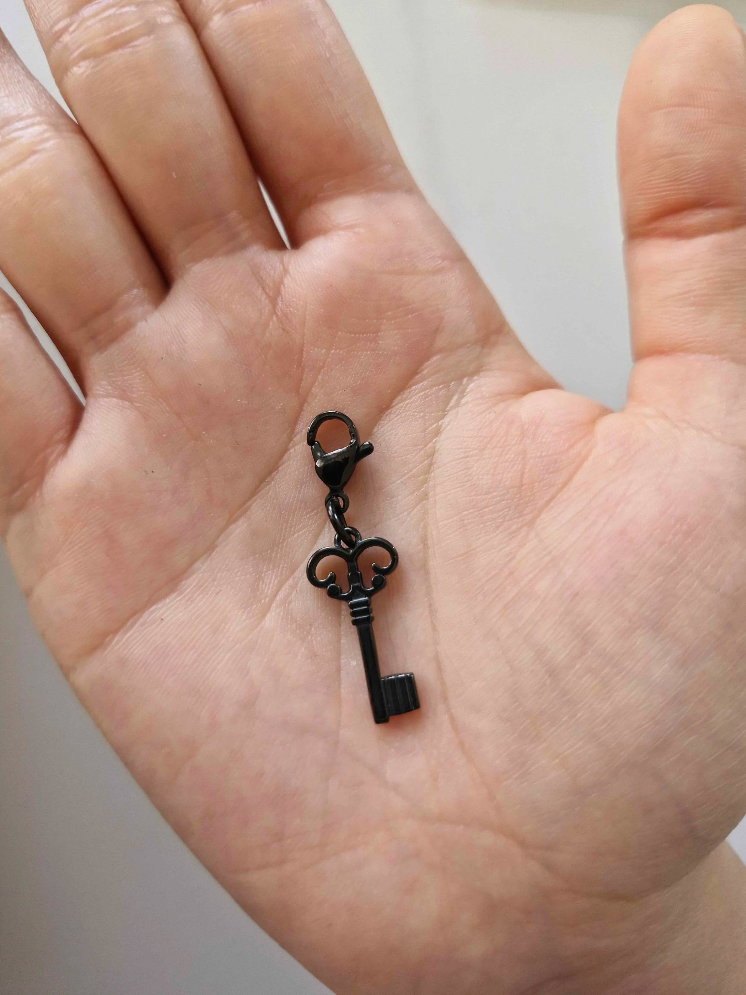 Black stainless-steel key charm resting on a hand to show scale | Celestia’s Charms