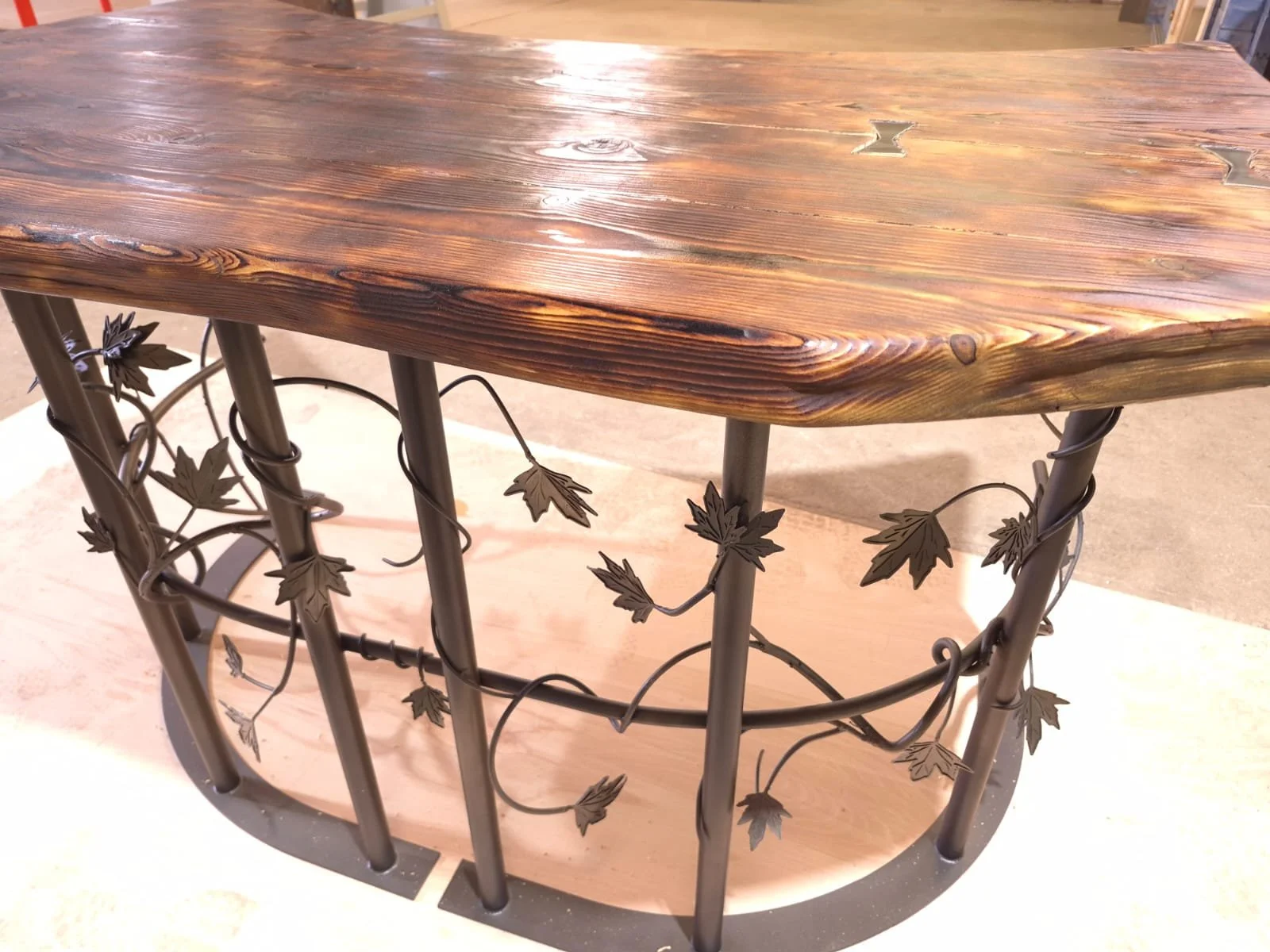 A wooden-top table with a decorative metal base featuring metal leaves and vines.