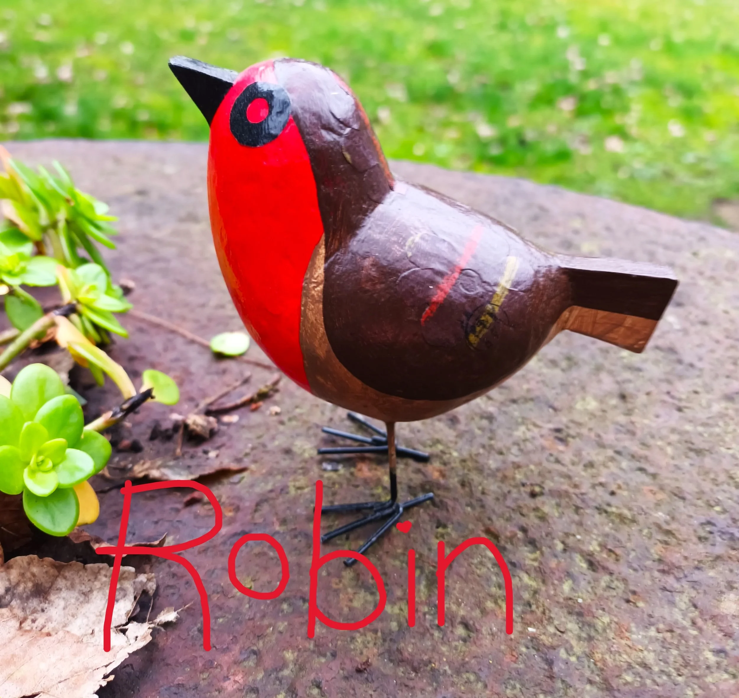 A small Posh Paper Mache mixed media Robin garden bird sculpture standing on a metal table, photographed in the artists garden.