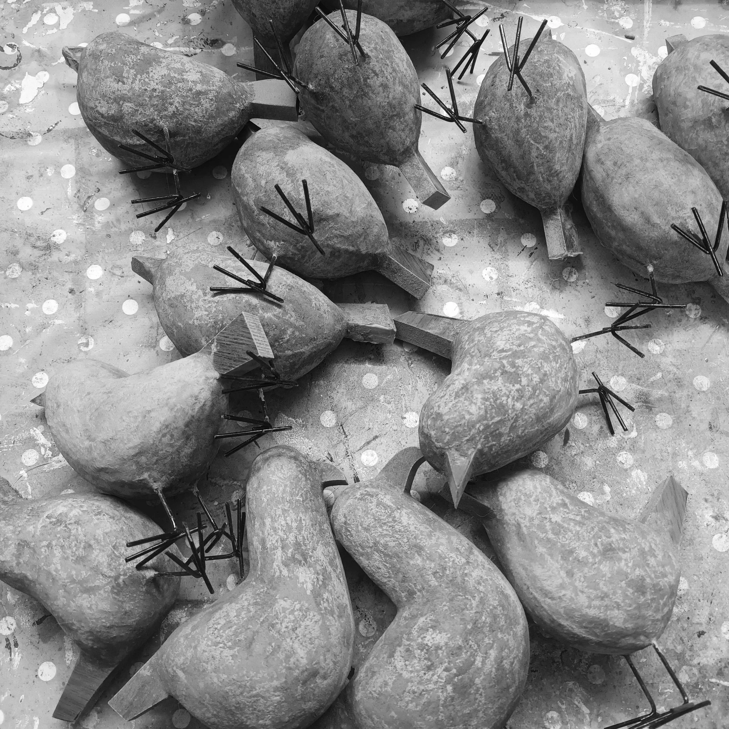 Black and white image of unpainted Posh Paper Mache birds with metal legs, scattered on a polka-dotted surface.